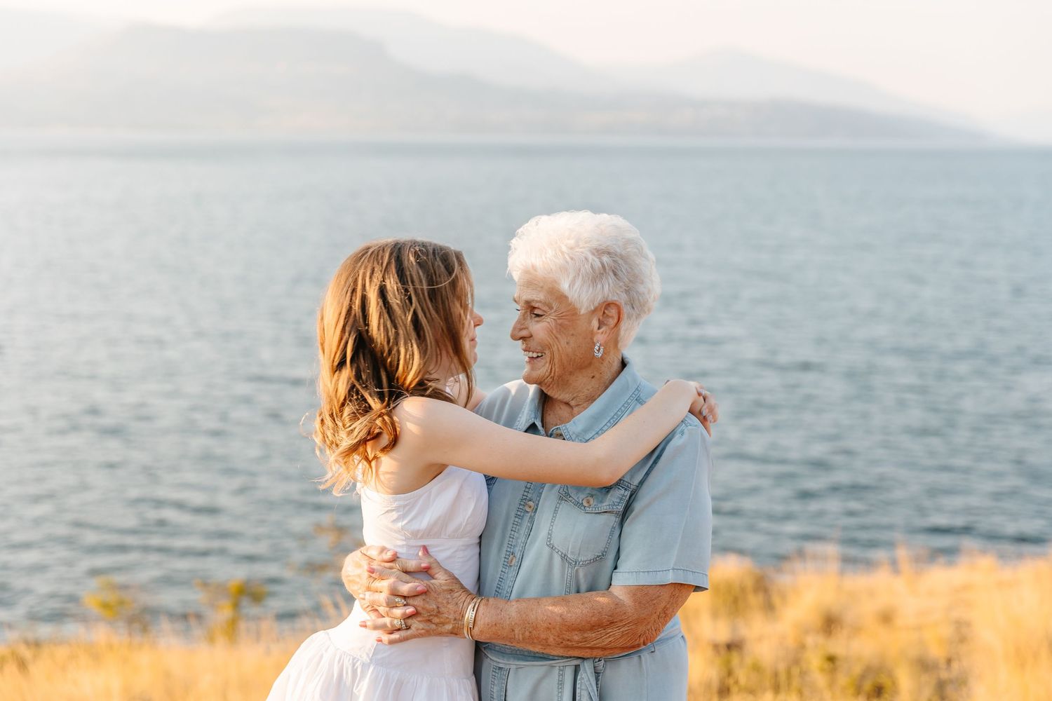 Romantic couple embracing on a grassy cliff overlooking the ocean during golden hour sunset.