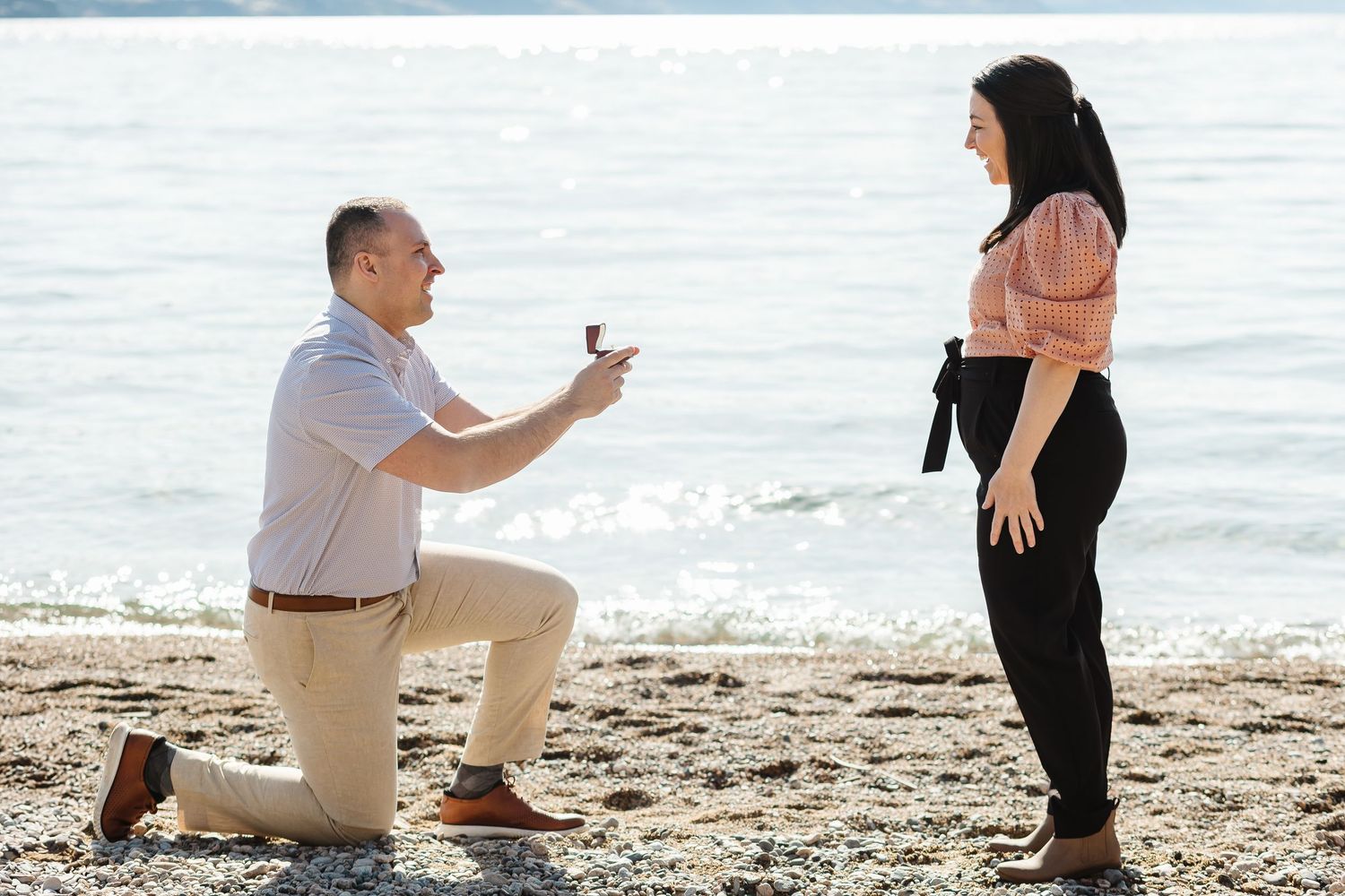 A romantic beach proposal scene unfolds as someone kneels in the sand at sunset to present a ring.