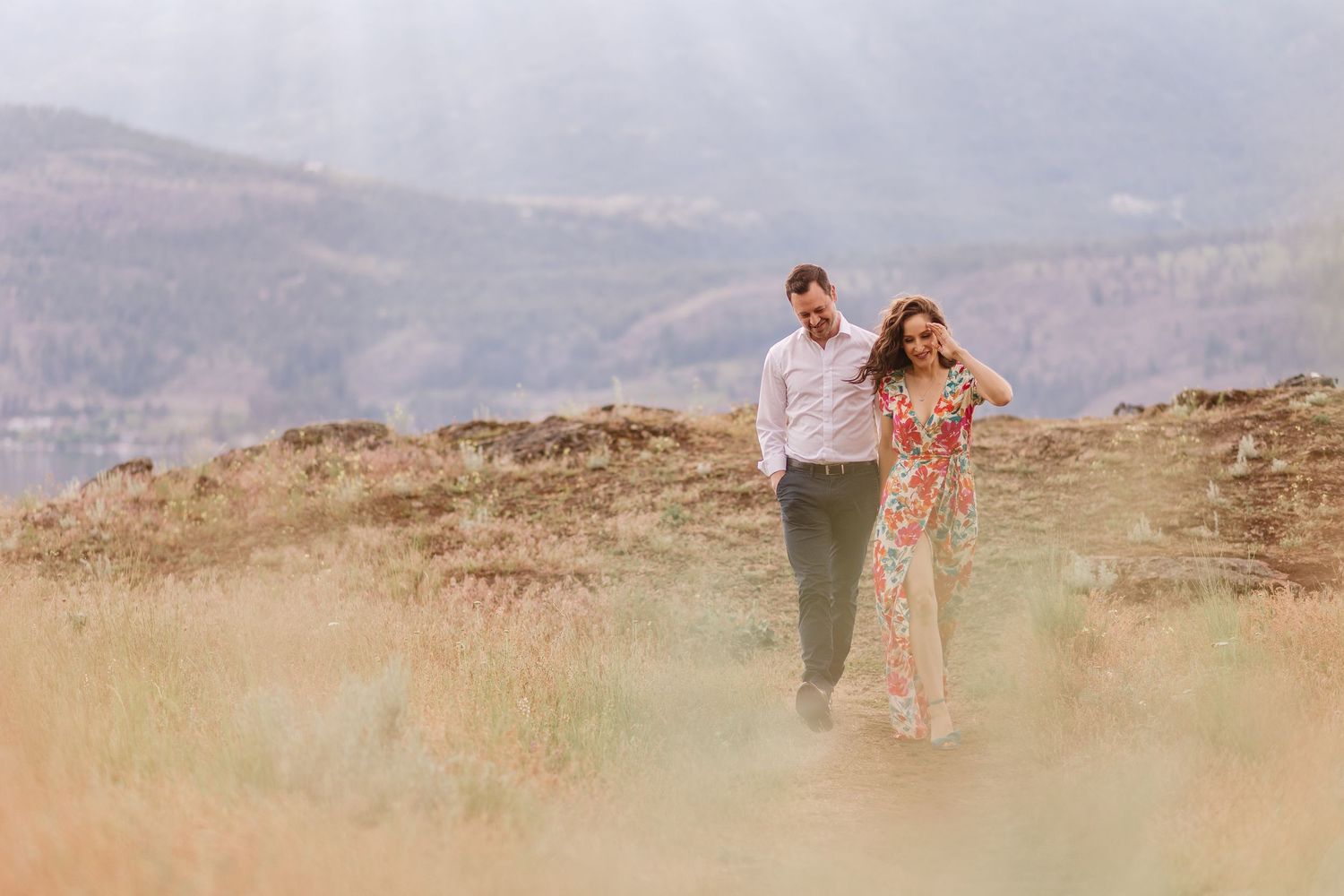 A couple walks along a scenic mountain trail during sunset, creating silhouettes against the golden landscape.