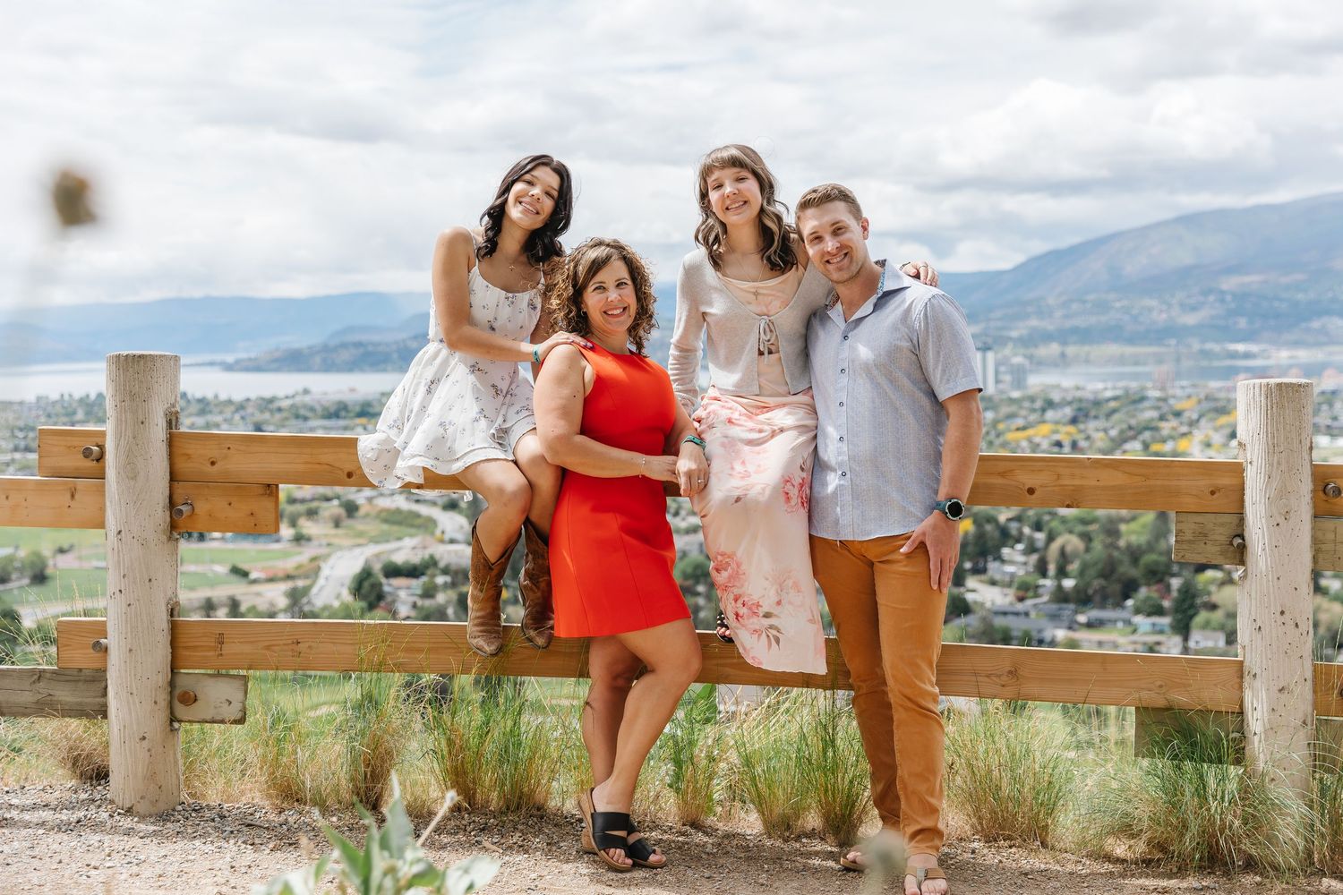 A group poses together at a scenic mountain viewpoint overlooking a valley on a cloudy day.