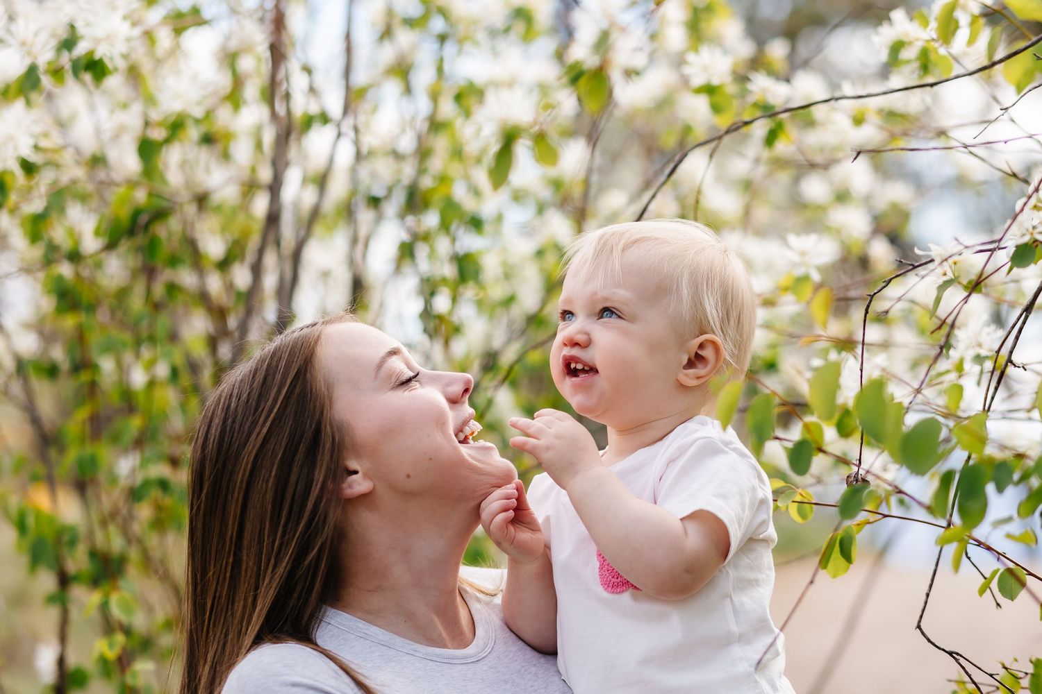 A parent and child share a joyful moment together outdoors among blooming spring tree branches.