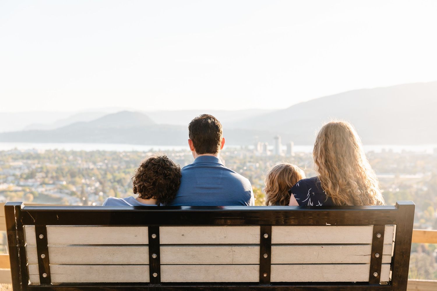 Group of people sitting on a bench overlooking a scenic mountain and city vista on a clear day.