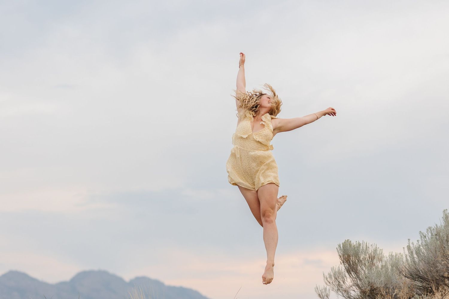 A dancer in a beige leotard performs graceful leaps and poses against a desert landscape at sunset.