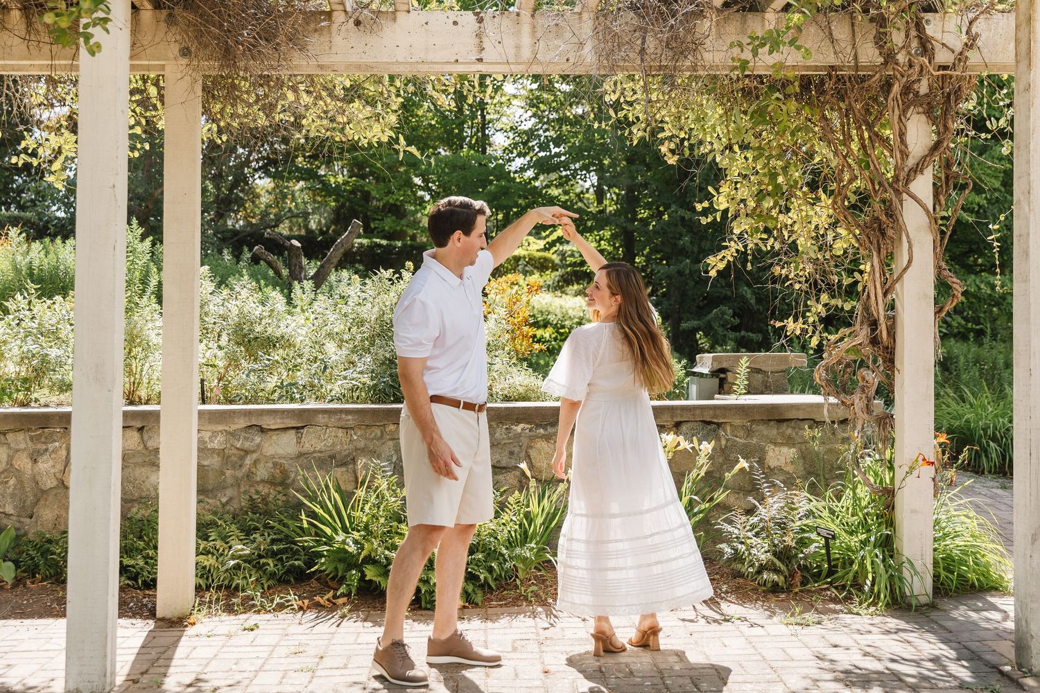 A stone colonnade walkway with arches in a garden setting during a sunny day.