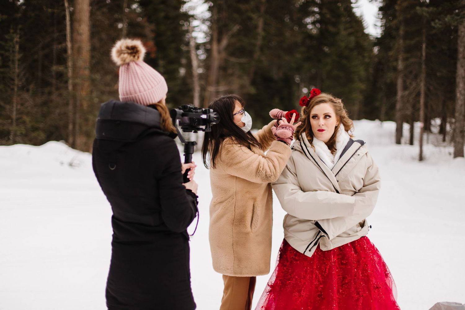 A couple embraces in a snowy winter forest setting while wearing formal attire and winter coats.