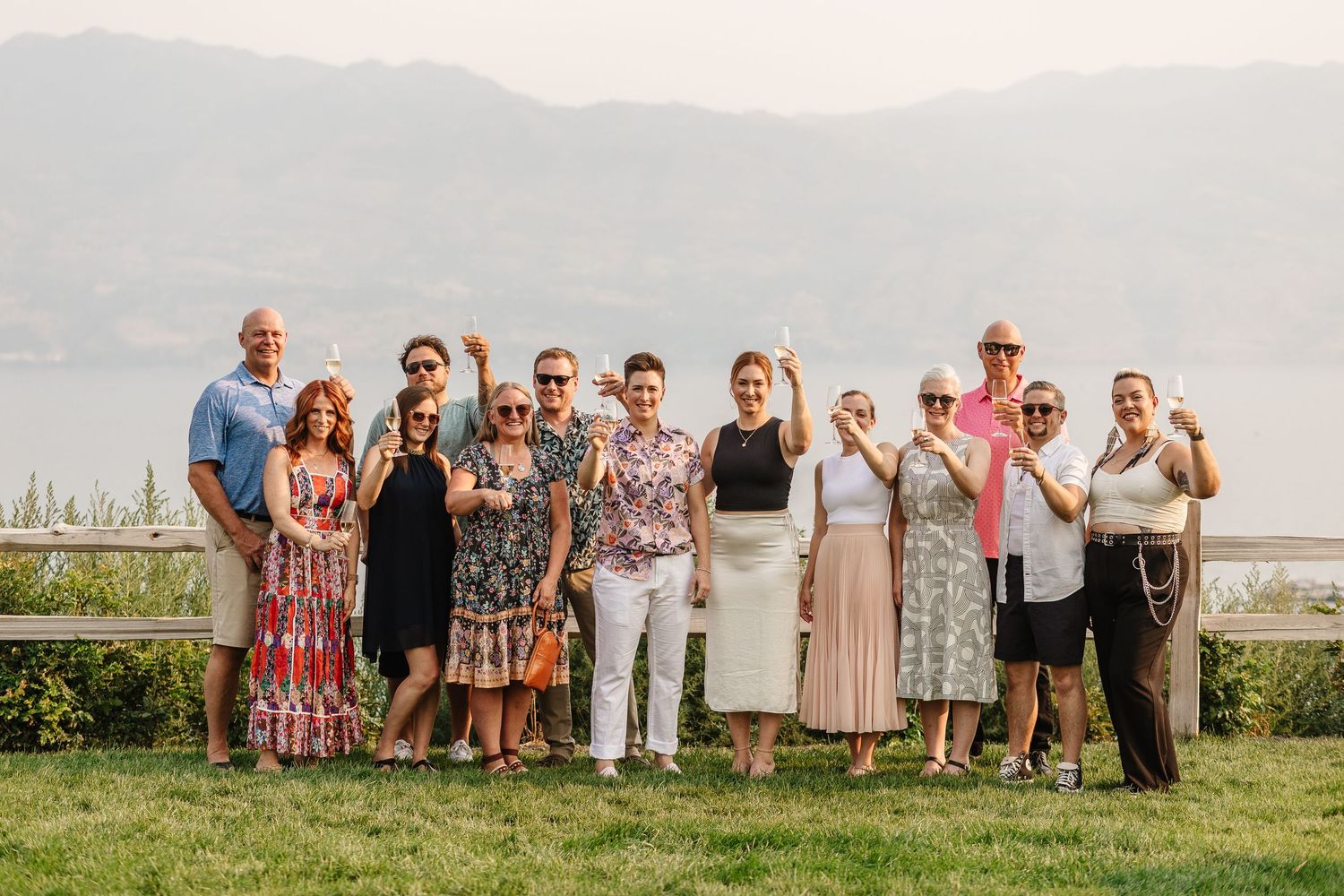 A group of people standing together outdoors with mountains and a lake in the background during golden hour.