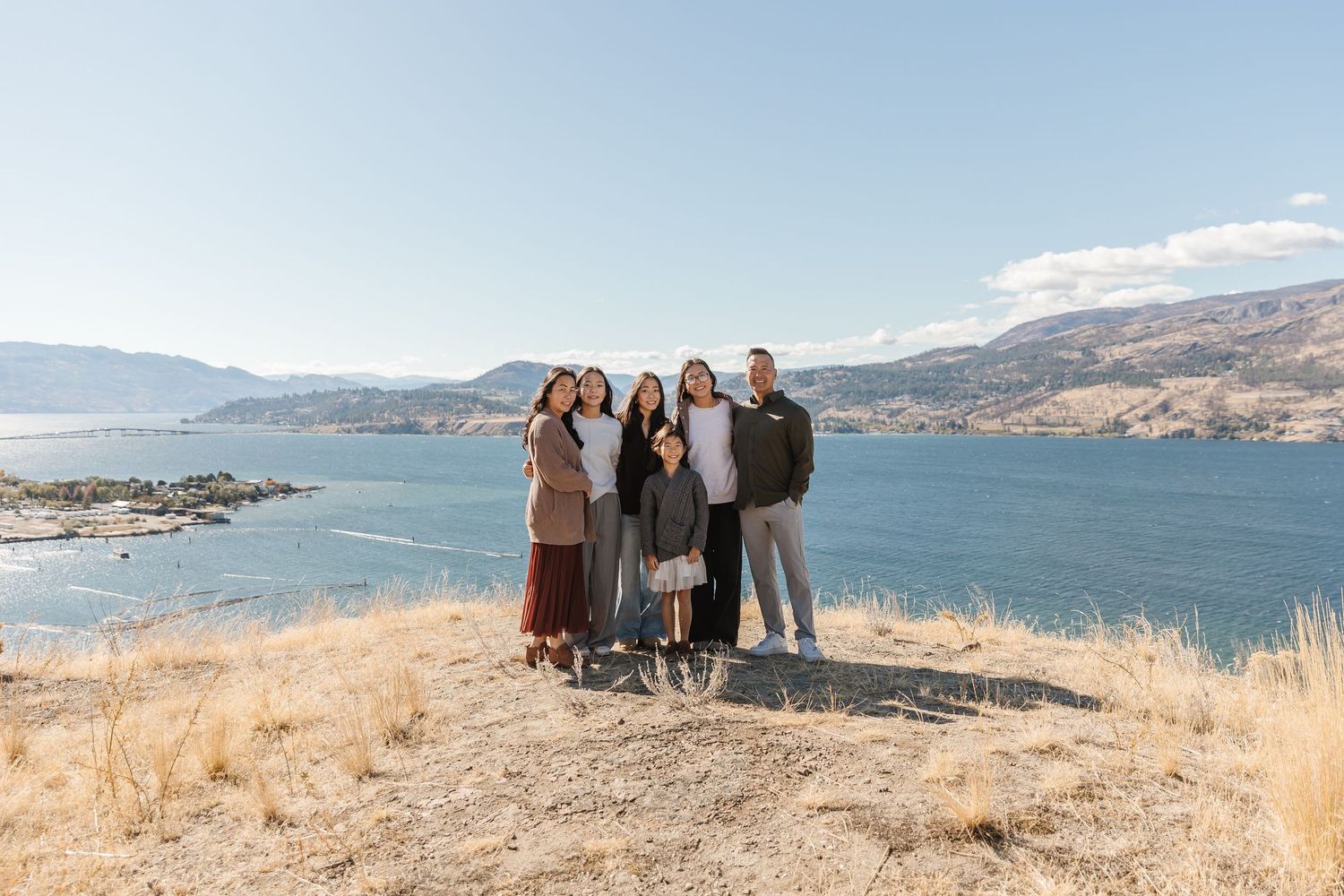 A panoramic view of people enjoying a scenic overlook at a lake surrounded by golden hills and mountains.