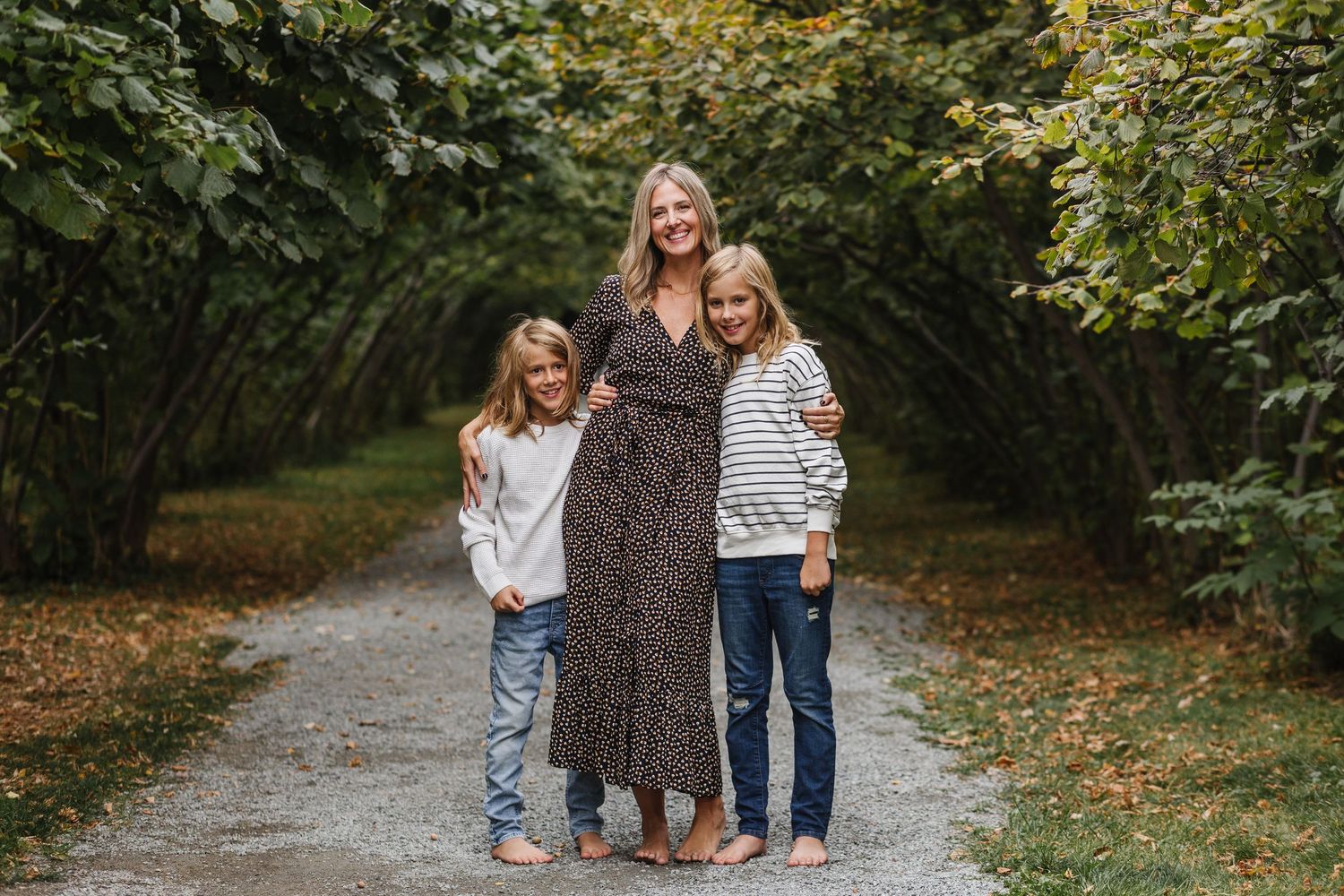 A family group stands together on a tree-lined gravel path during autumn.
