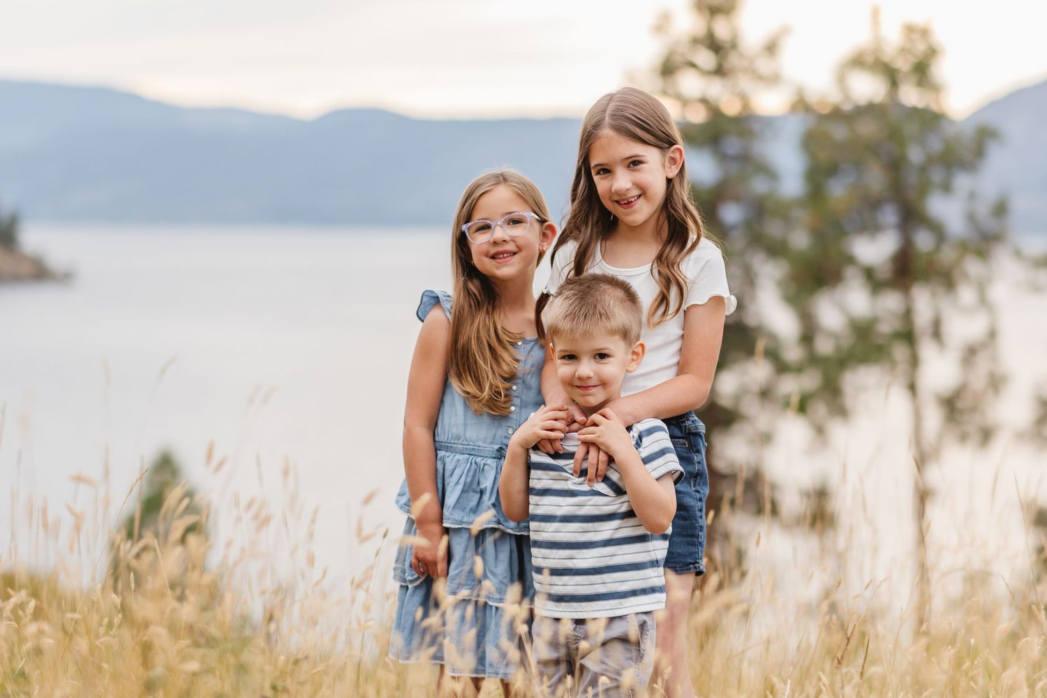 A family wearing coordinated blue and white outfits poses together in a scenic mountain meadow at sunset.