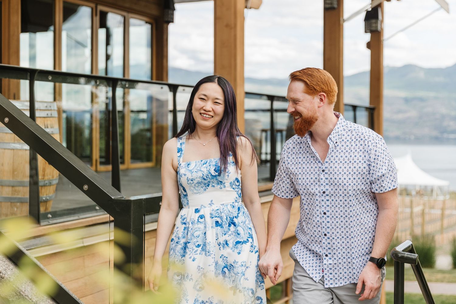 A couple in blue and white outfits share romantic moments at a scenic overlook with mountain and lake views.