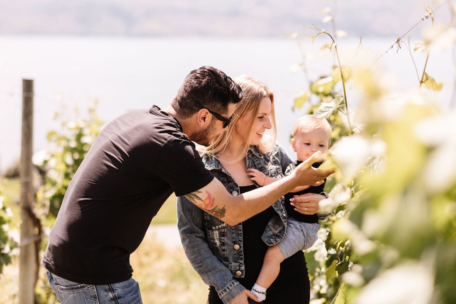 A parent lifts and embraces a small child in a sunny outdoor setting with trees and natural light.