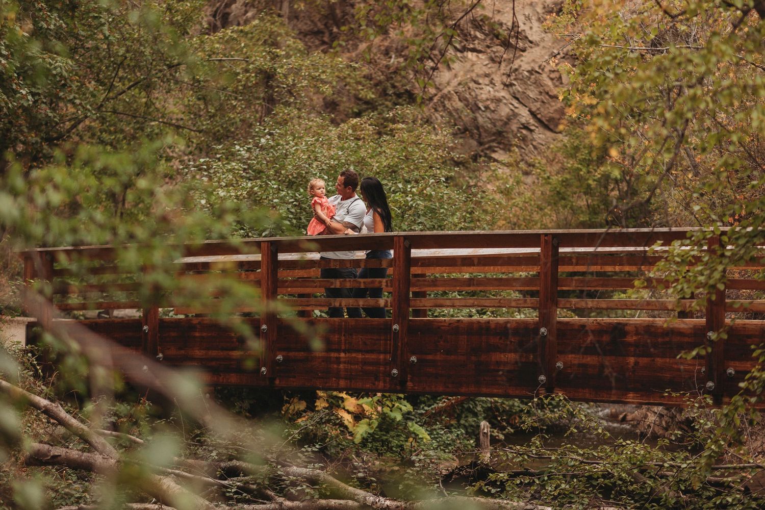 A wooden bridge spans across a creek in an autumn forest with colorful fall foliage reflecting in the water.