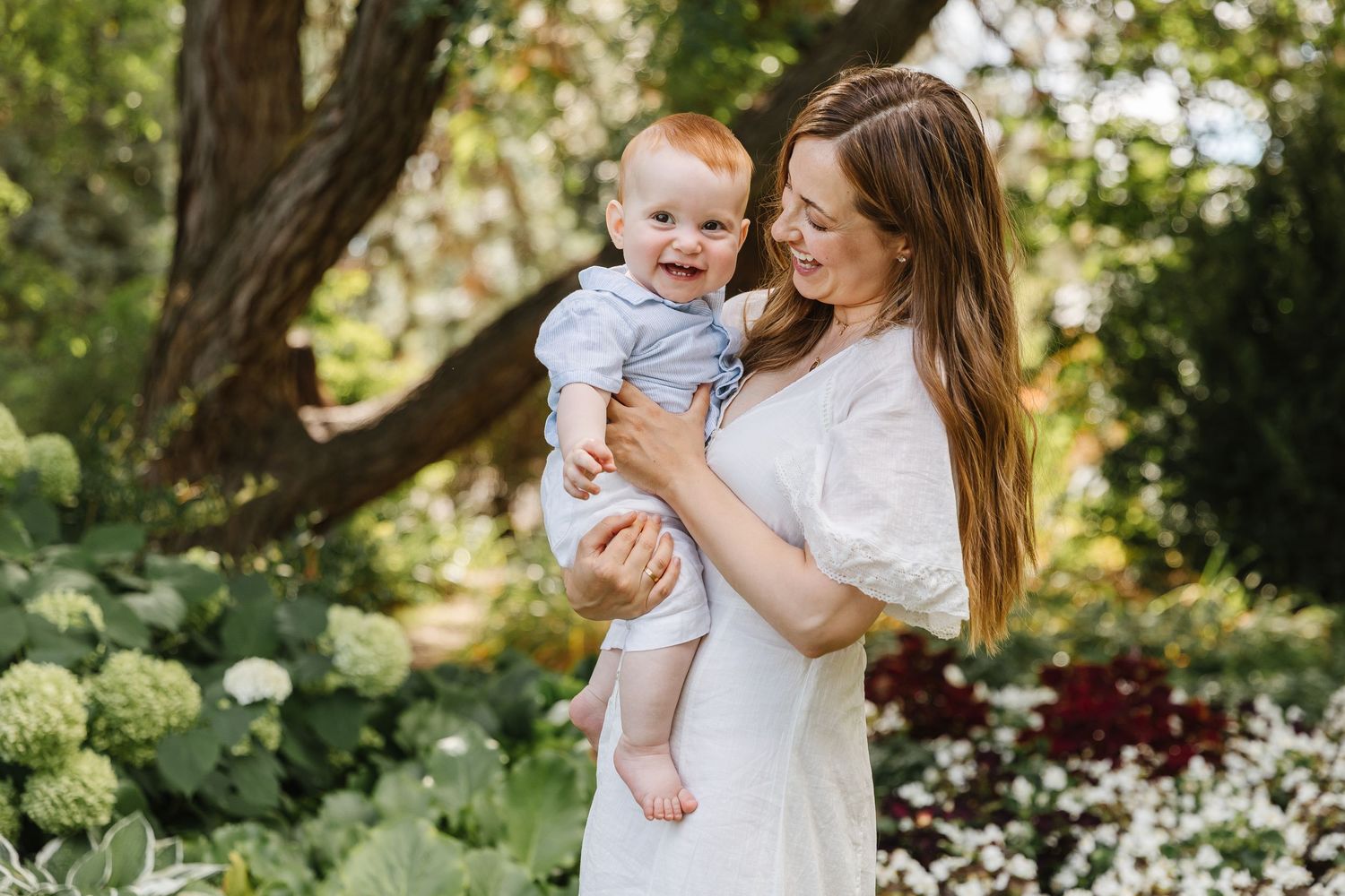 A tender family moment captured in a lush garden setting with blooming flowers and greenery.