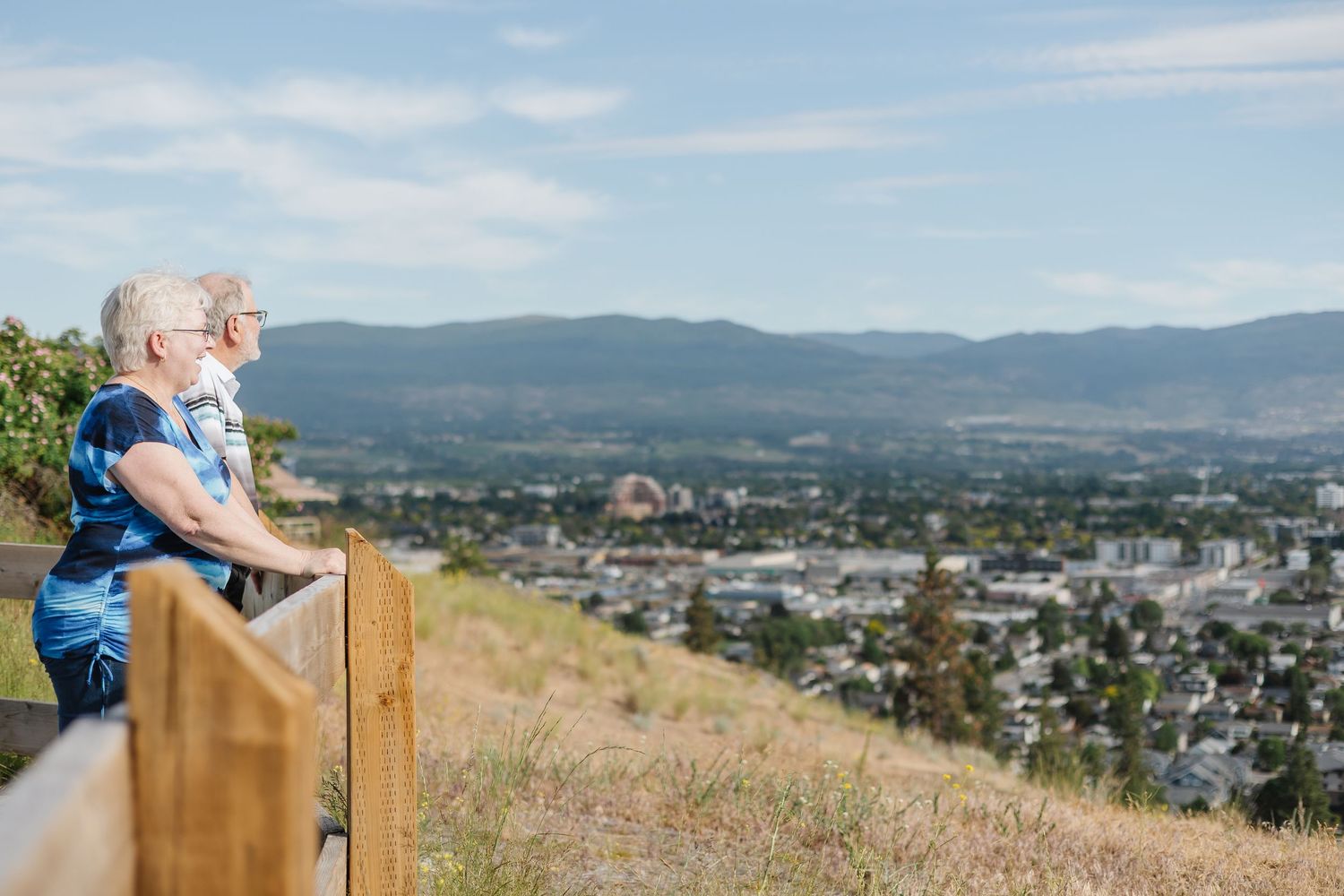 Scenic panoramic view of a city nestled in a valley with mountains in the background and a person sitting on a bench.