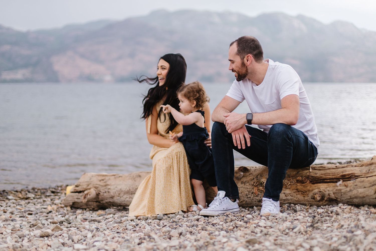 Couple sitting together on rocky coastal shoreline with ocean and cliffs in background during sunset.