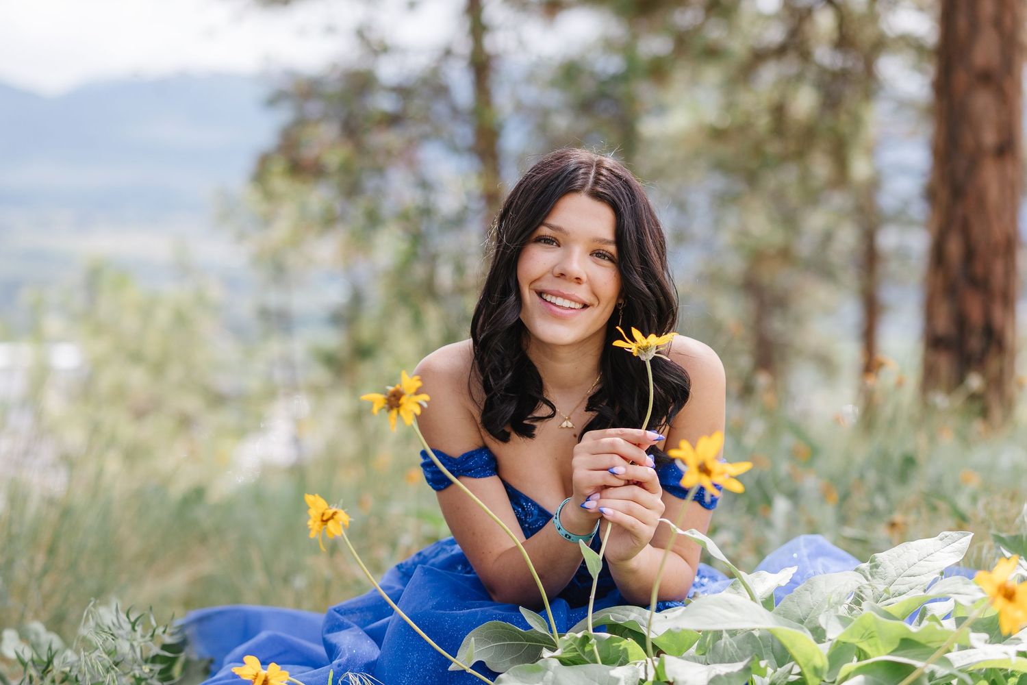 Person in bright blue sweater sits in a meadow of yellow wildflowers on a sunny day.