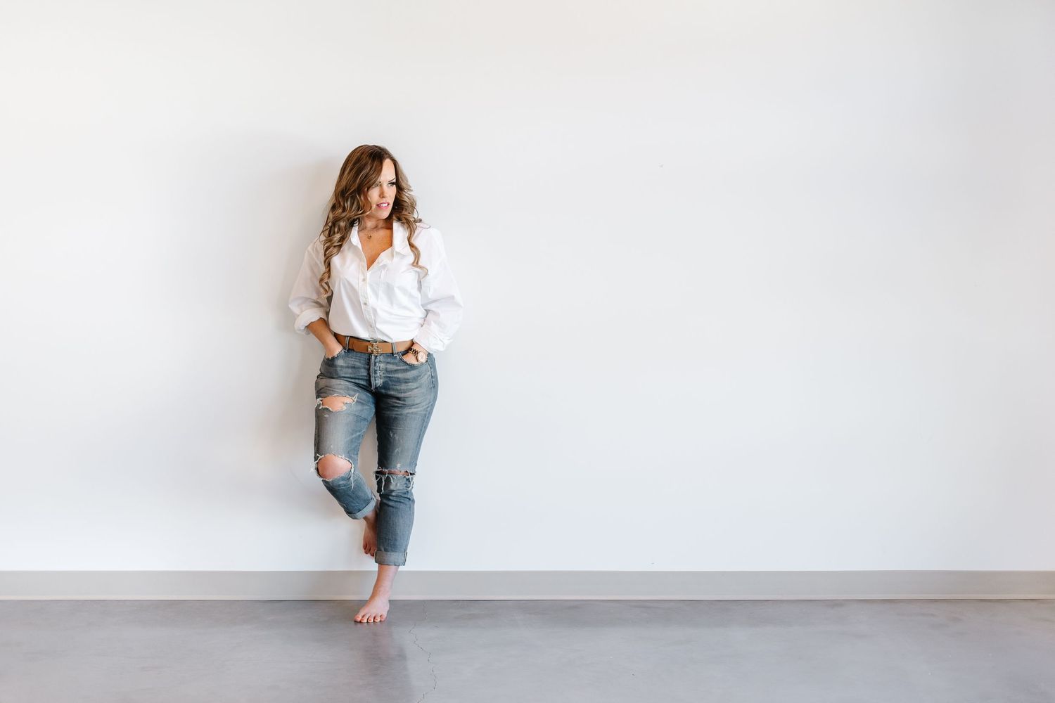 Woman in white top and light blue jeans poses against white wall in five casual lifestyle shots.