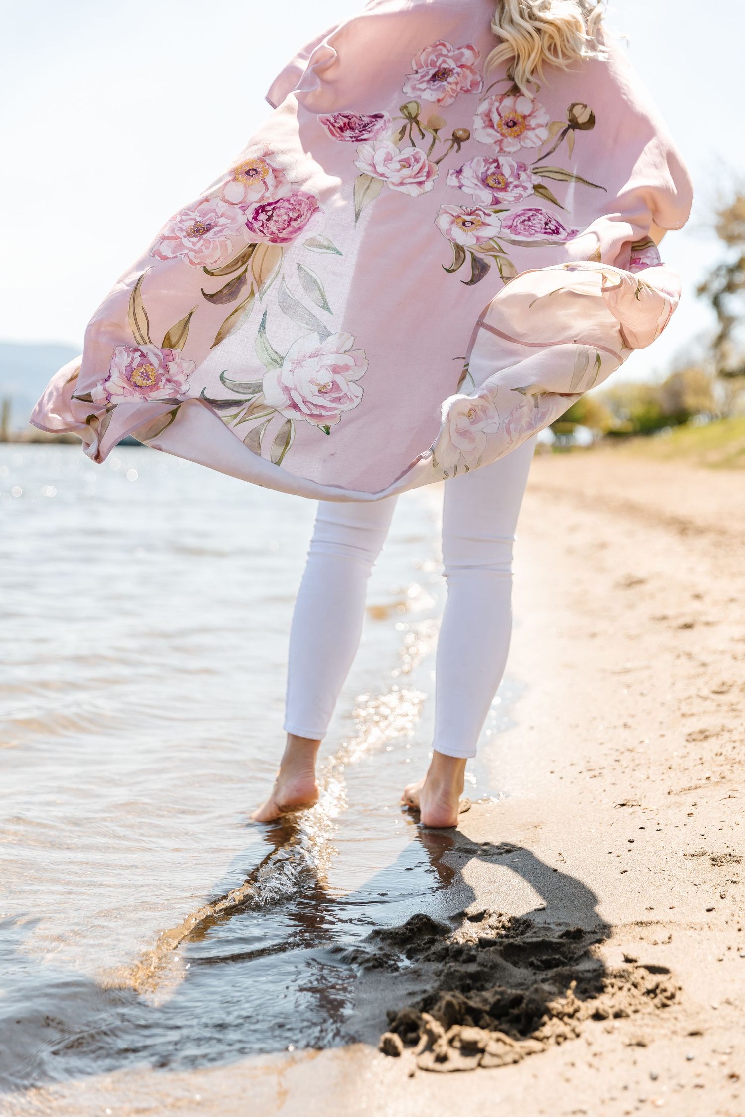 A person wearing a floral dress and white pants stands at the water's edge in Osoyoos at the watermark resort for a women's retreat