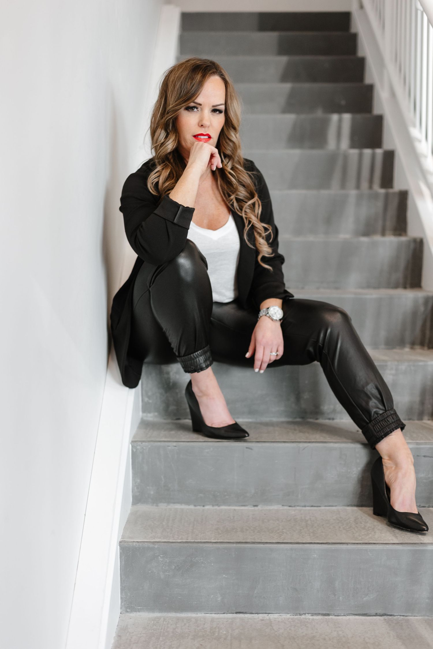 Professional fashion model in black blazer and red lipstick poses elegantly on concrete stairs.