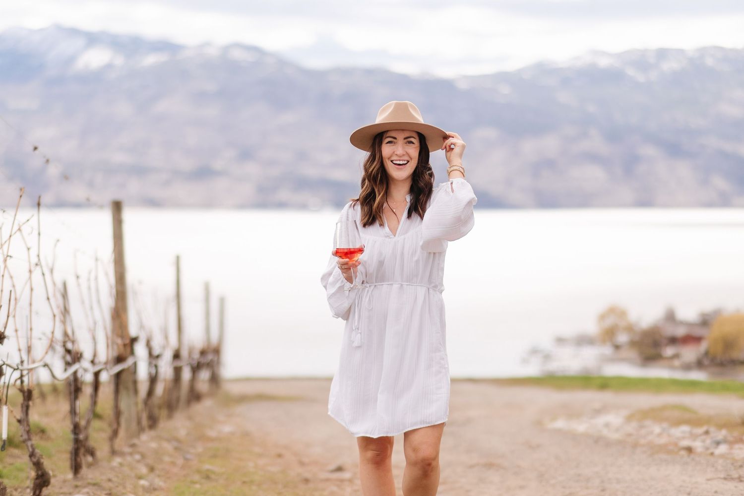 A person in a white dress walks through a scenic mountain landscape on a sunny day.