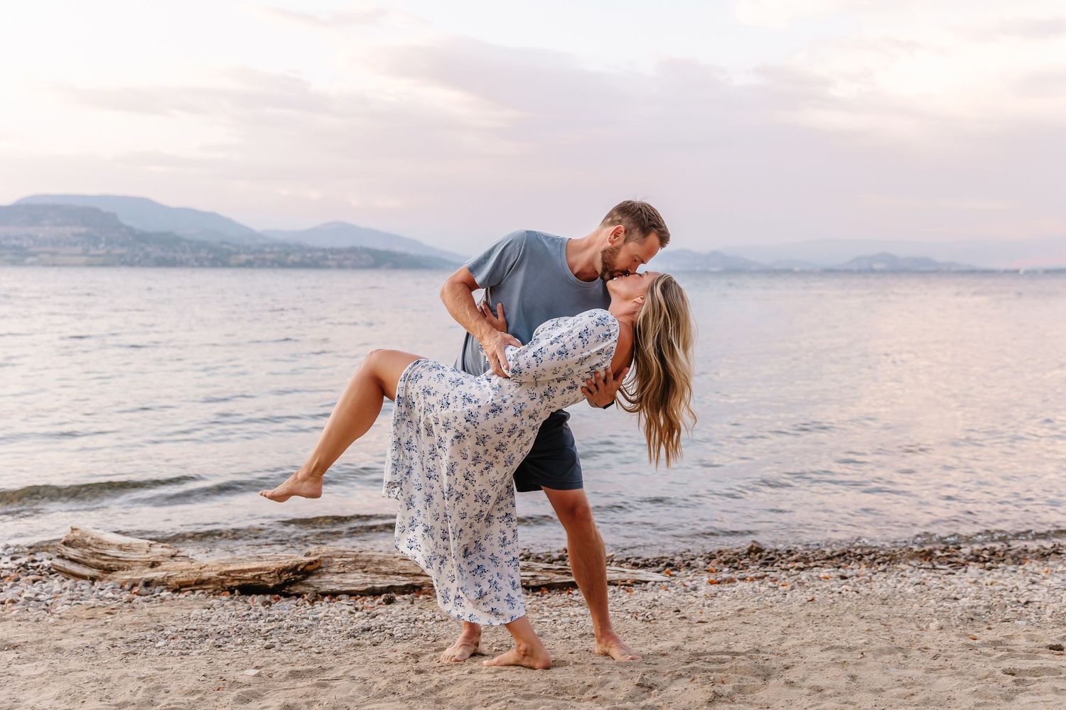 A couple shares romantic moments on a beach at sunset while taking photos against the scenic ocean backdrop.