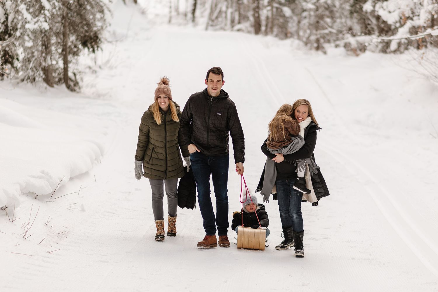 A group walks together down a snowy winter path while carrying a basket on a cold day.