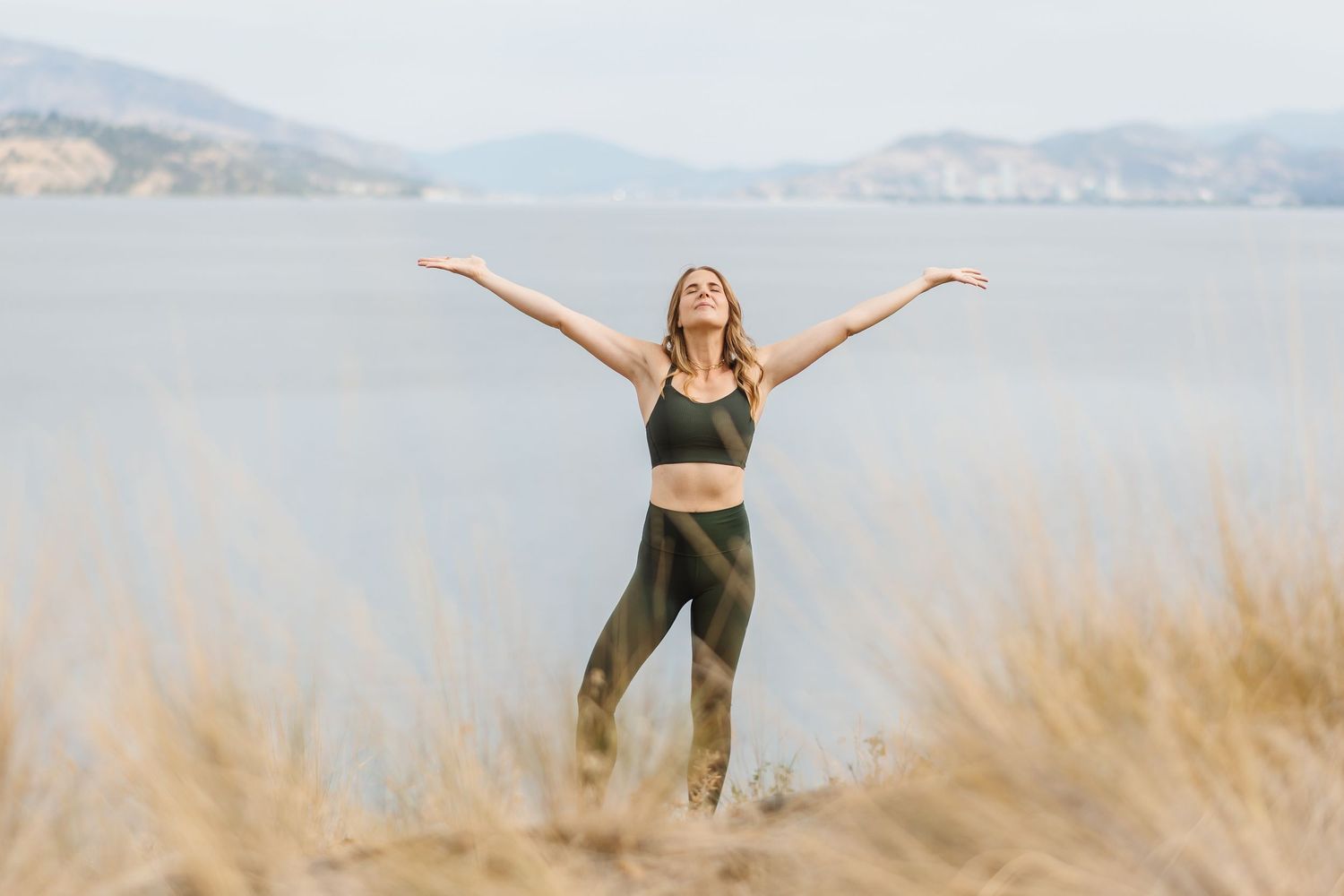 Person striking joyful poses on a scenic beach with mountains and ocean in the background.