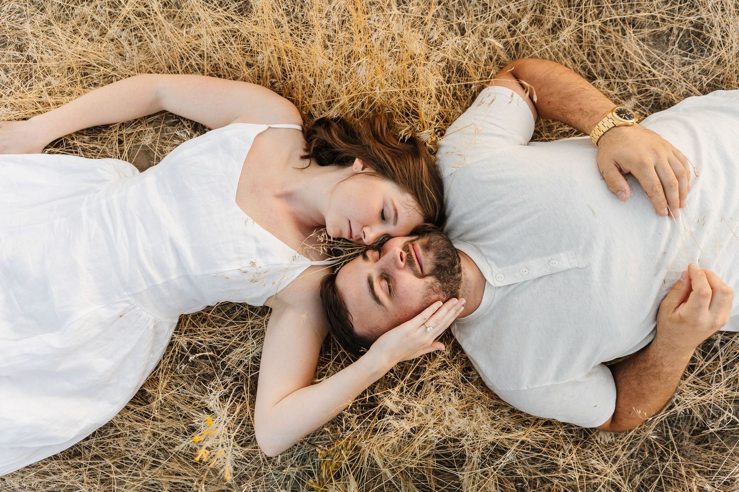 Someone in a white dress lies gracefully in golden grass during a dreamy outdoor photo session.