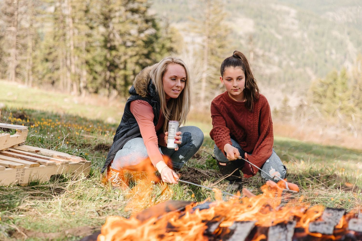 People enjoying a cozy campfire gathering in nature while sitting on blankets and preparing food outdoors.
