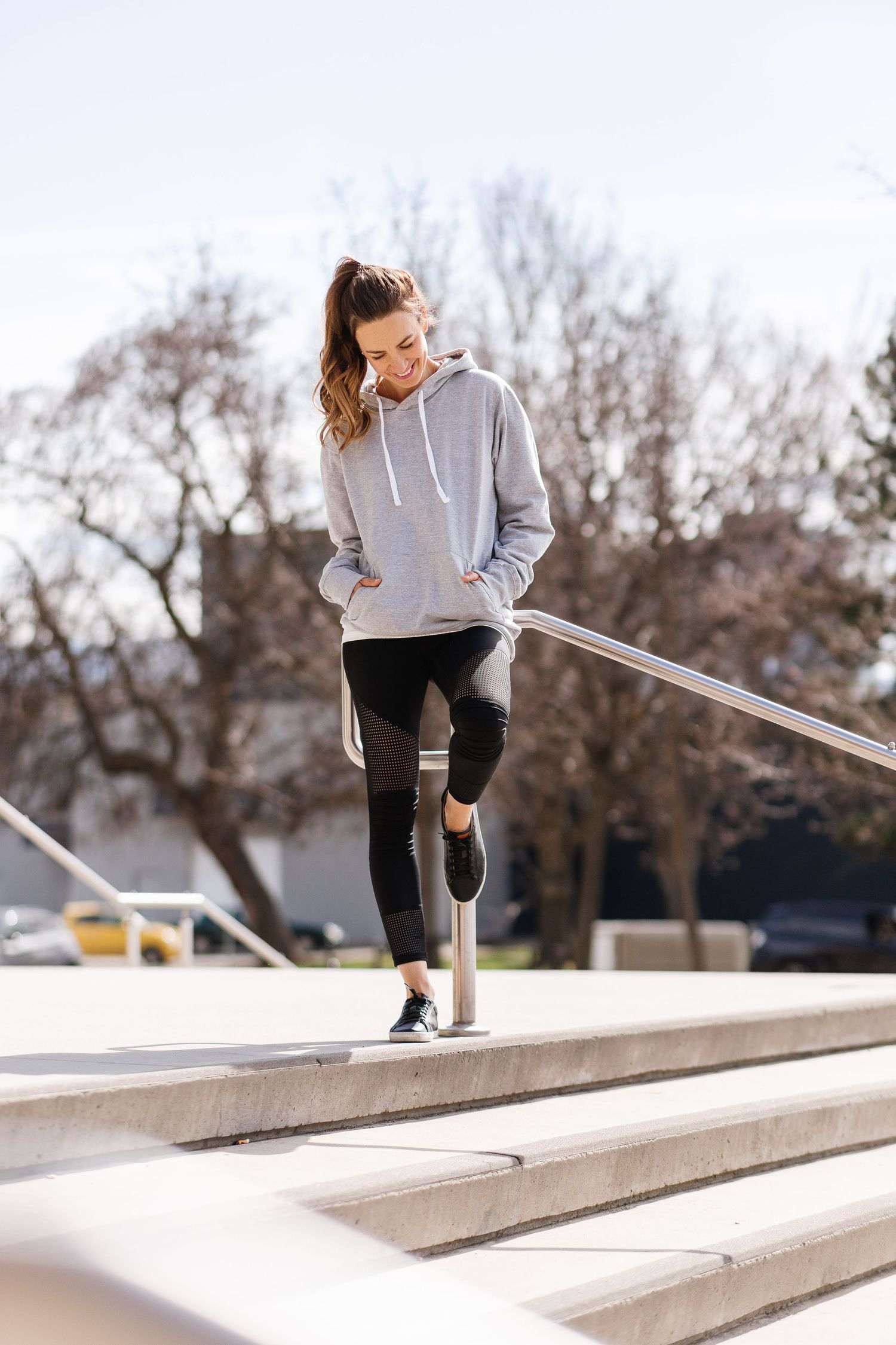 Athlete in gray sweatshirt and black pants performs stretching exercises on concrete steps outdoors.