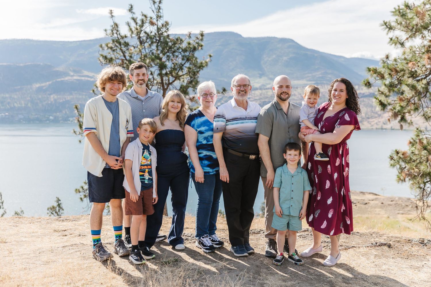 A group of people pose together on a scenic overlook with a lake and mountains in the background.