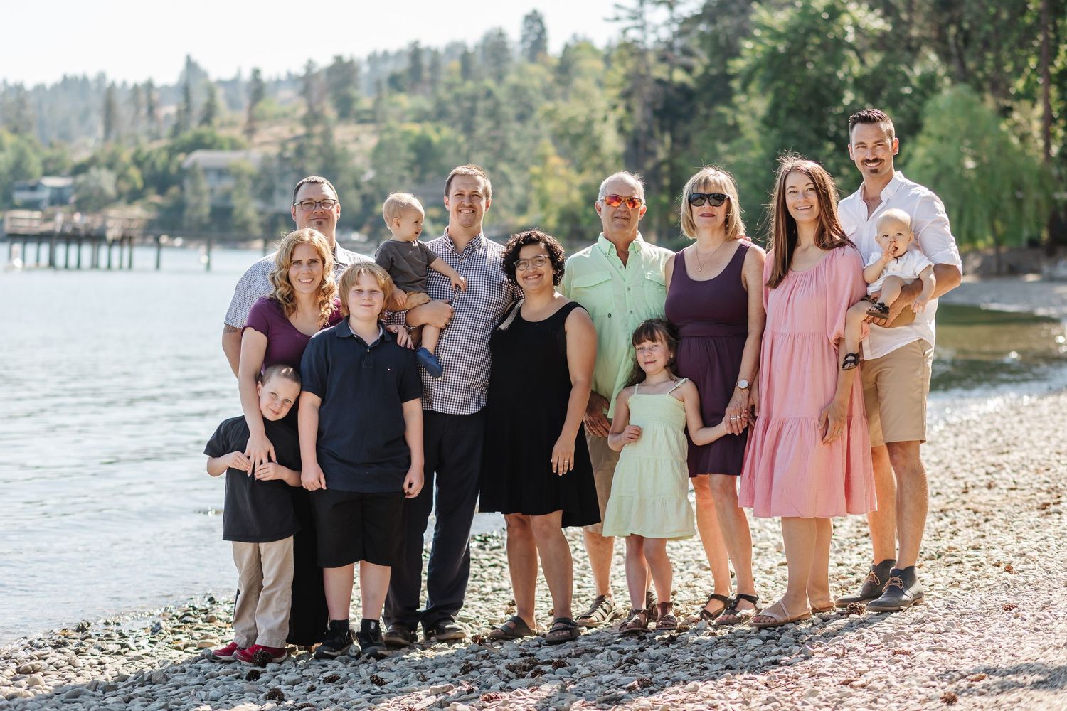 Group of people standing together on a rocky beach shoreline during sunset wearing coordinated formal attire.