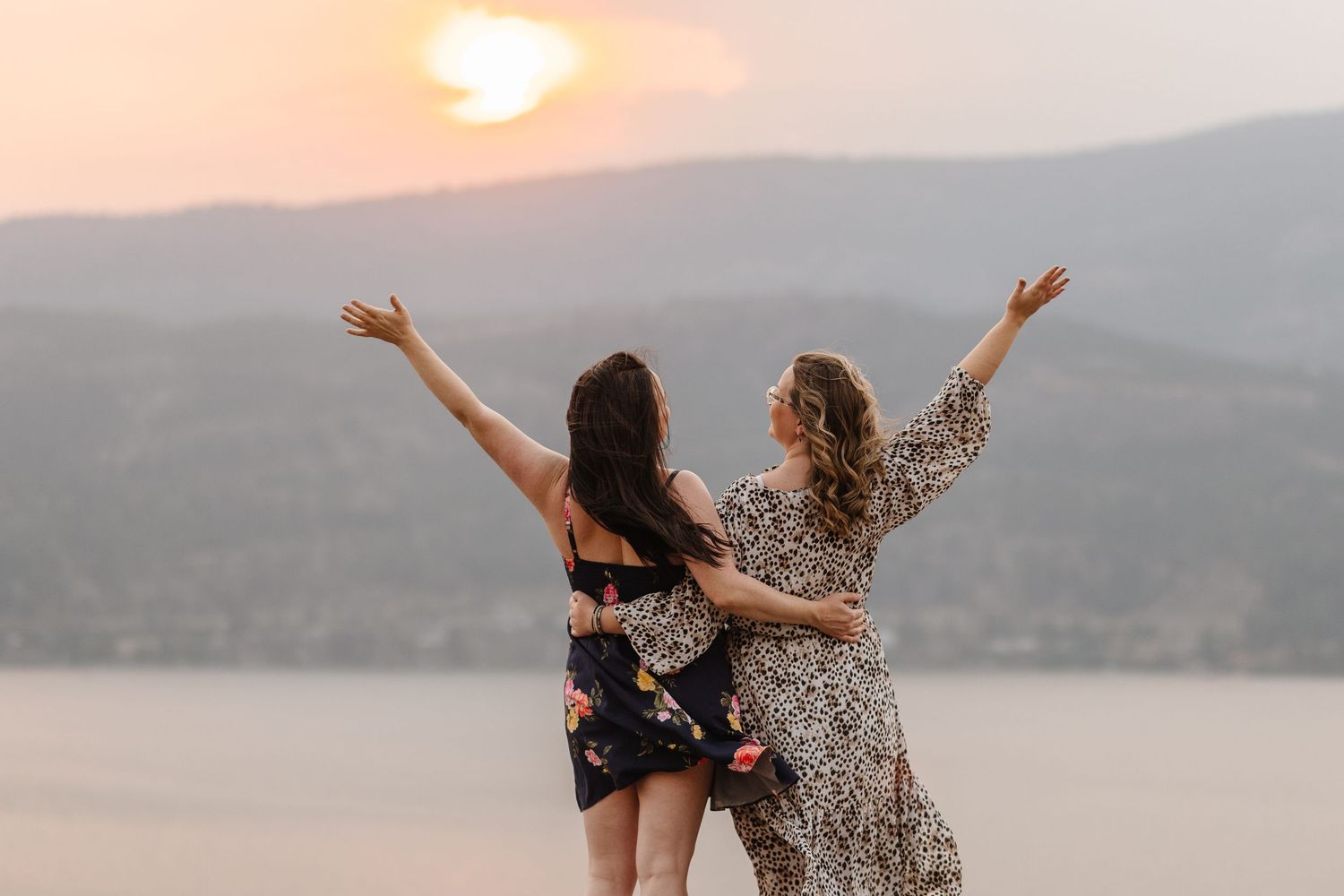Two friends celebrate with arms raised against a misty mountain backdrop during sunset.