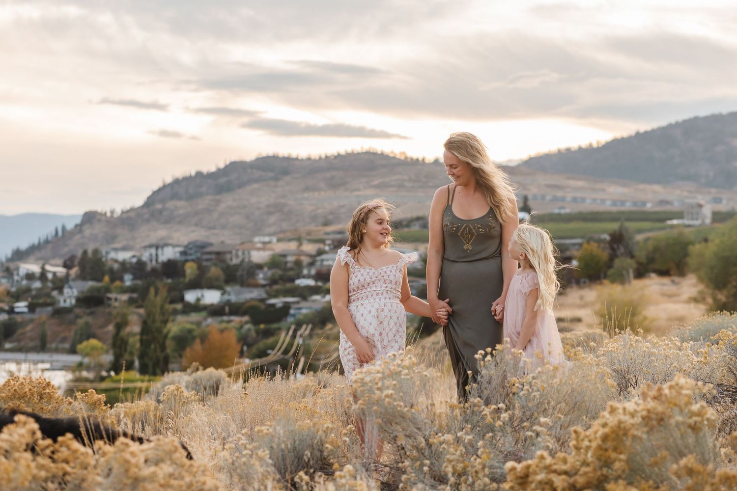 A couple walks through a scenic mountain landscape with golden grasses and dramatic clouds at sunset.