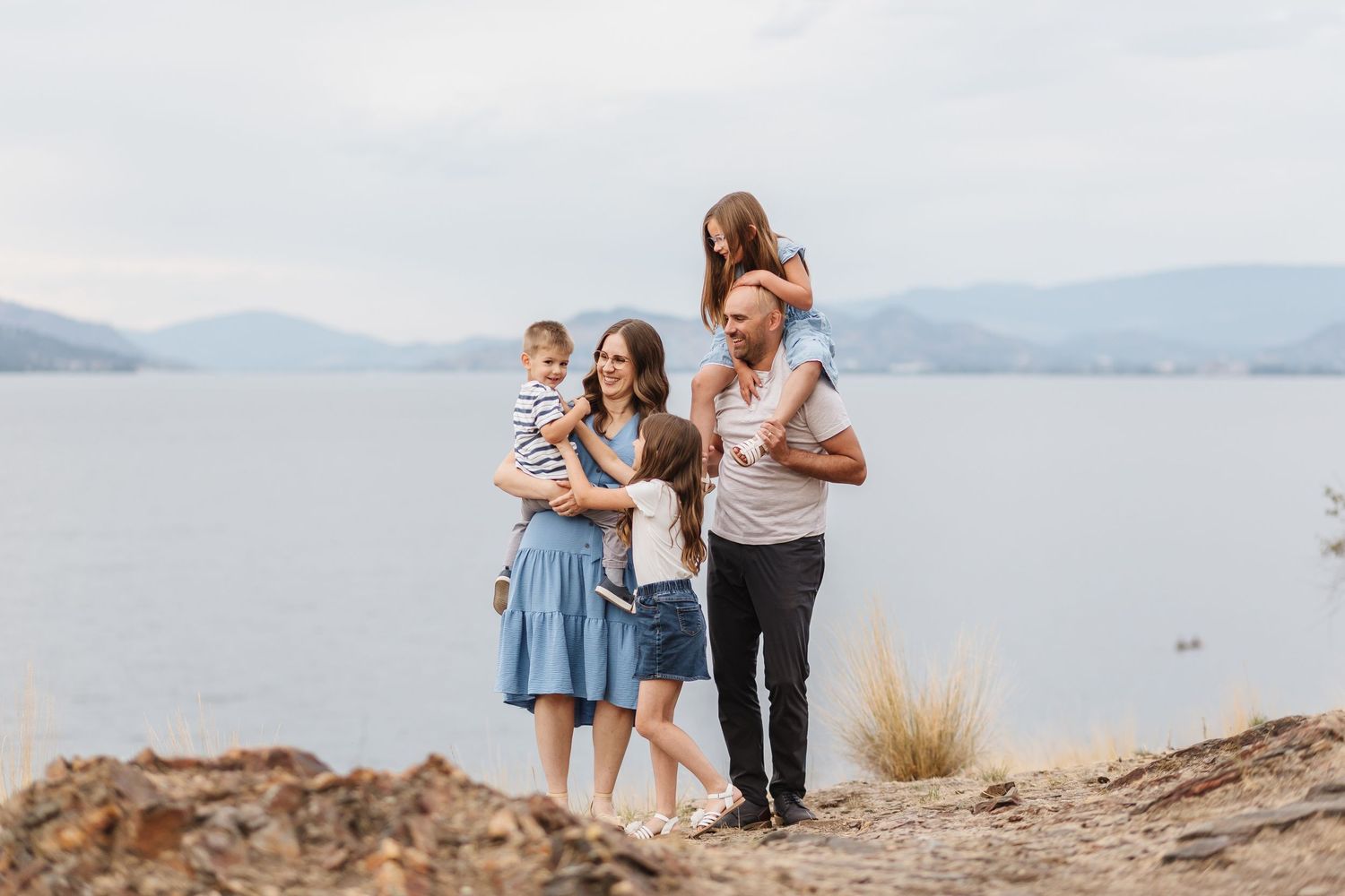 Family walking together along scenic mountain trail overlooking lake and mountains in summer.