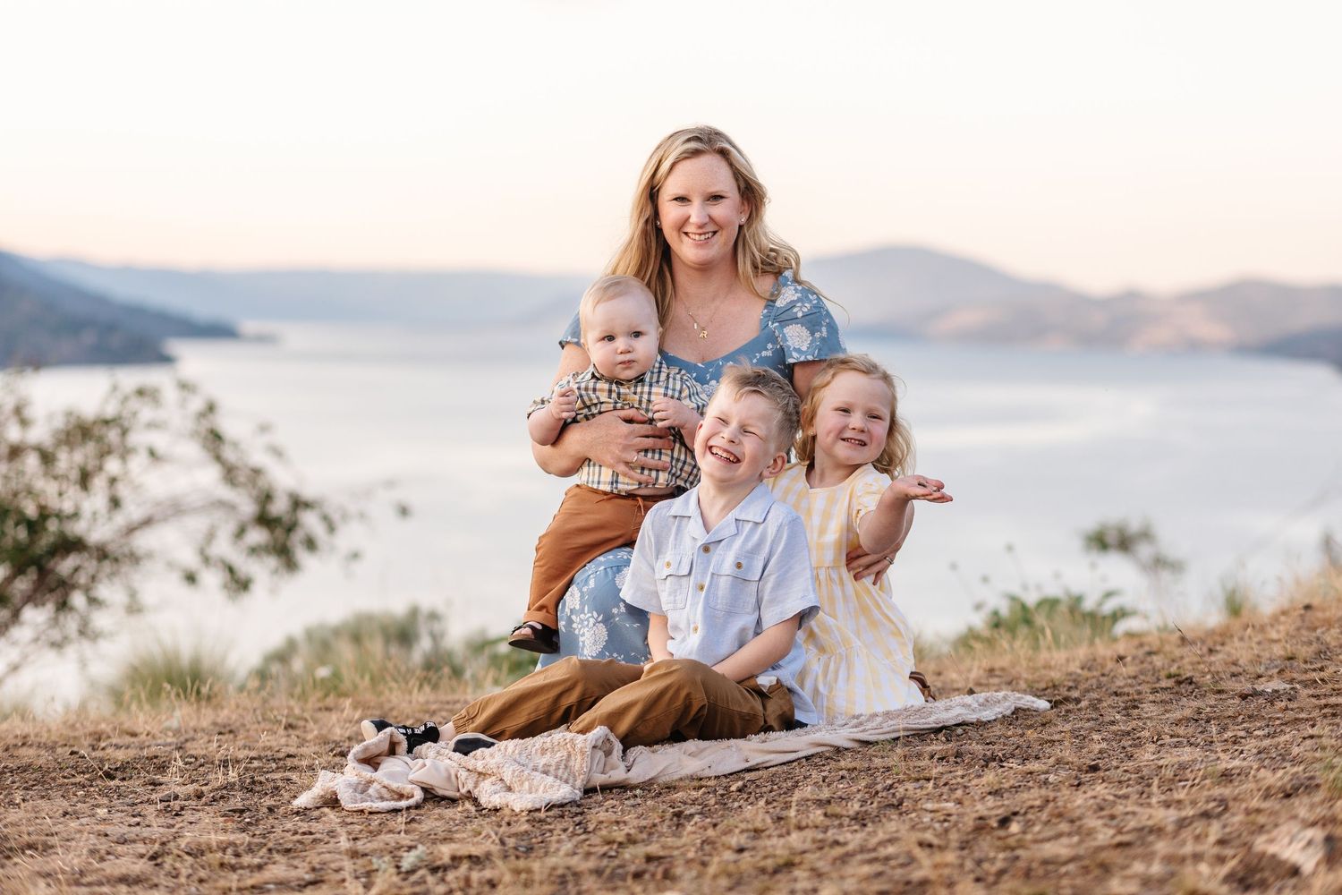 A series of candid outdoor family portraits taken at sunset on a hillside overlooking a scenic mountain lake.