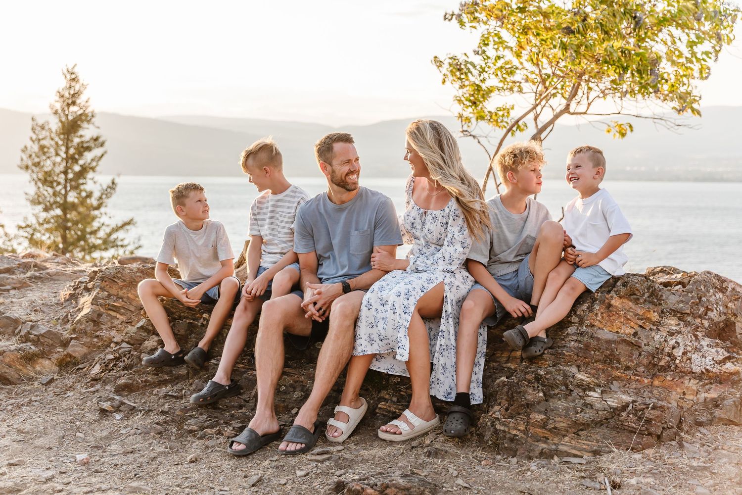 A group sits together on a rocky outcrop overlooking a serene lake at sunset with golden trees in the background.