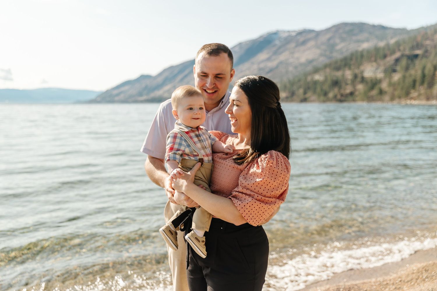 Family enjoying a sunny day together at a scenic mountain lake beach with gentle waves lapping at the shore.