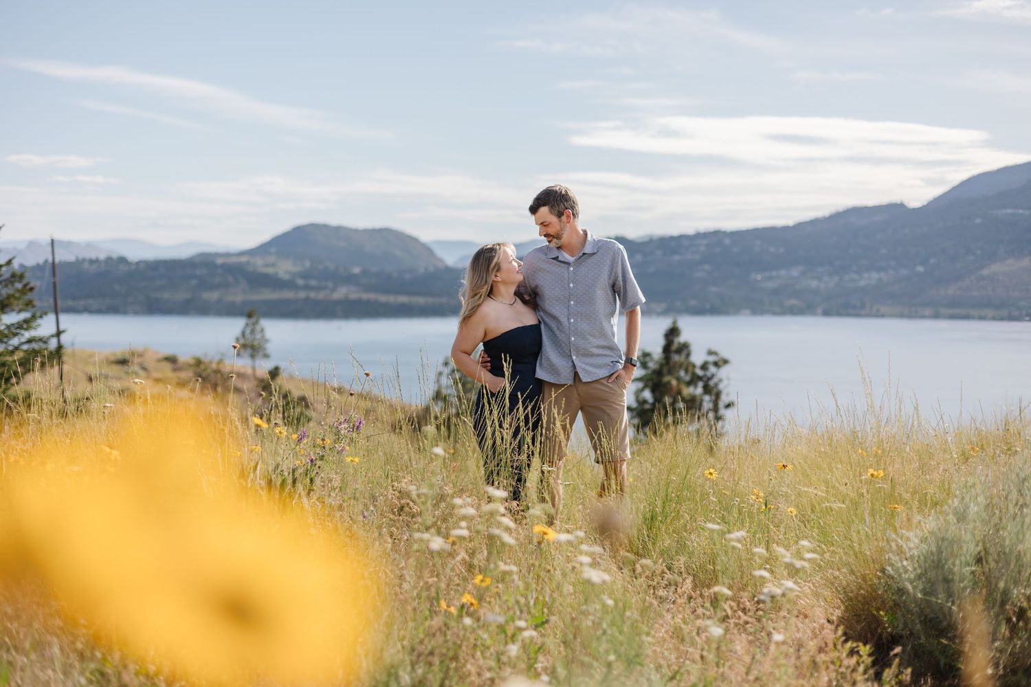 A couple shares a romantic moment on a hilltop overlooking a scenic lake and mountain landscape.