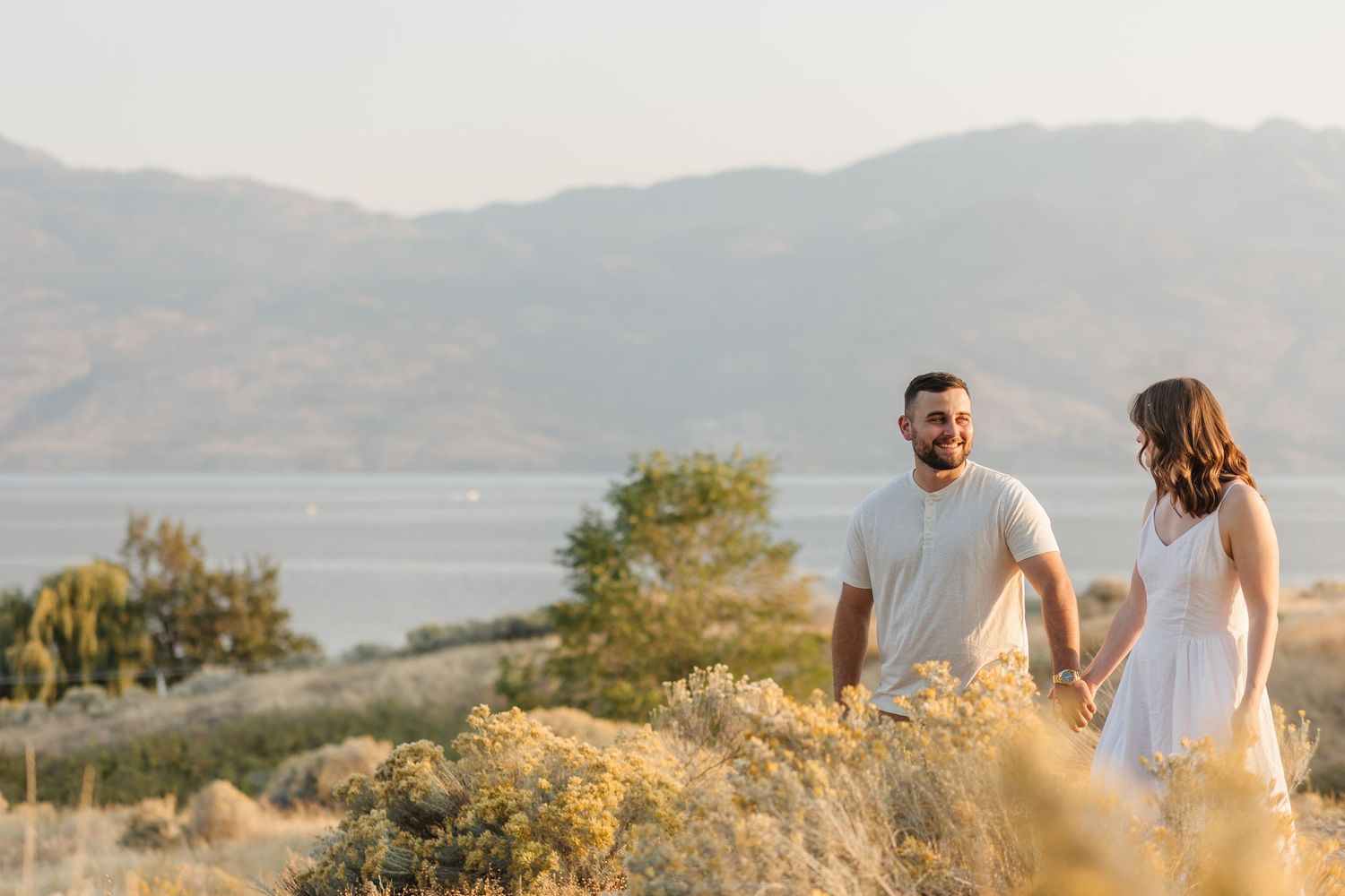Two people walk together on a hilltop path at sunset with mountains and golden light in the background.