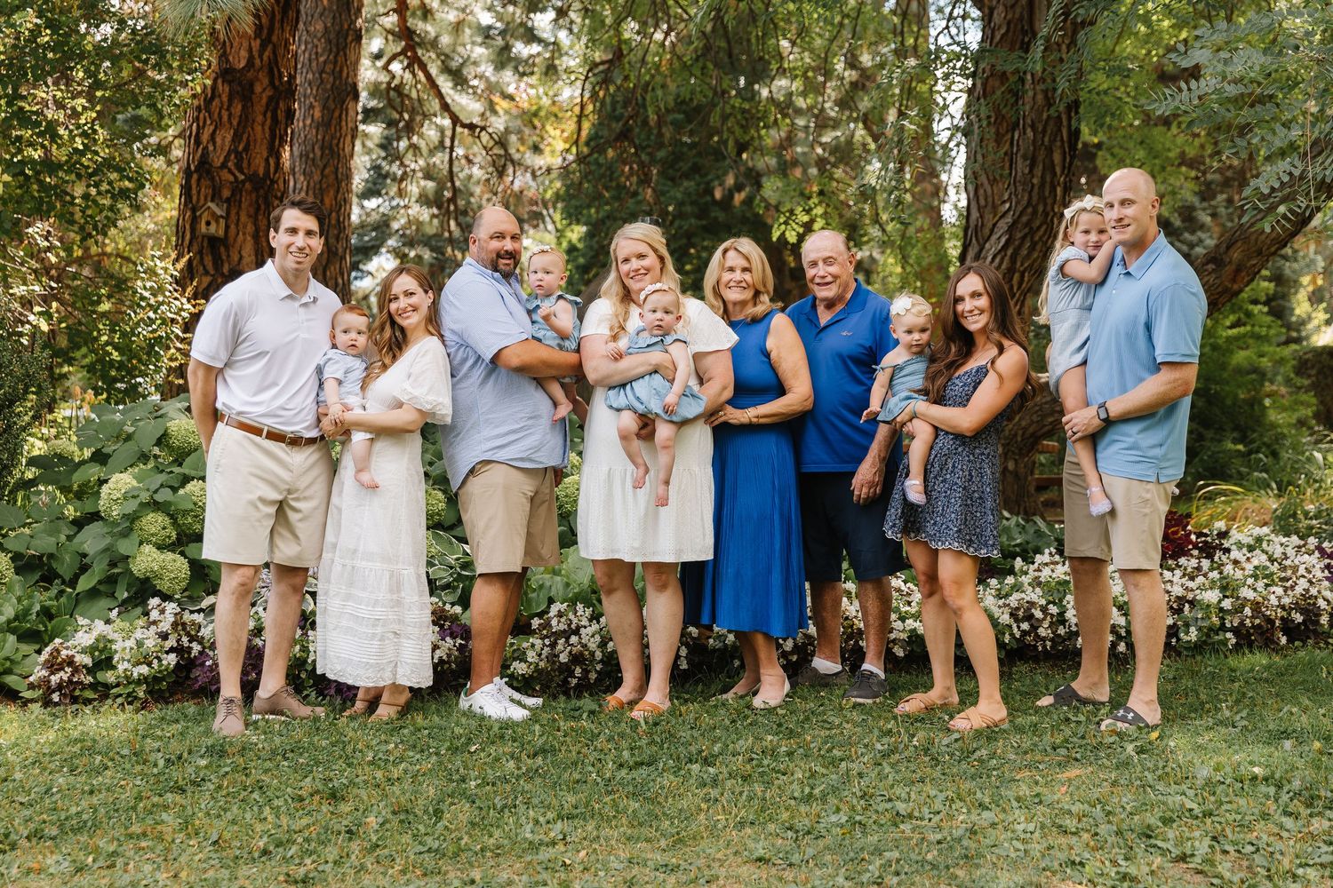 A group of people in coordinated white and blue outfits pose together outdoors in a garden setting.