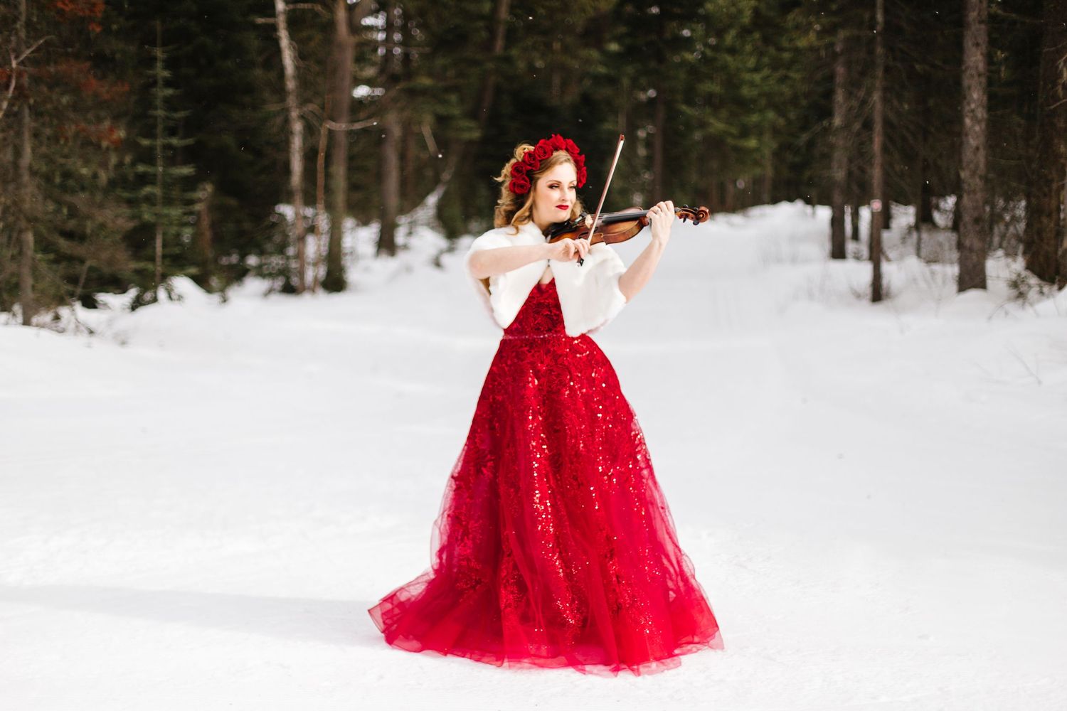 A figure in a flowing red ballgown poses gracefully in a snowy winter forest landscape.