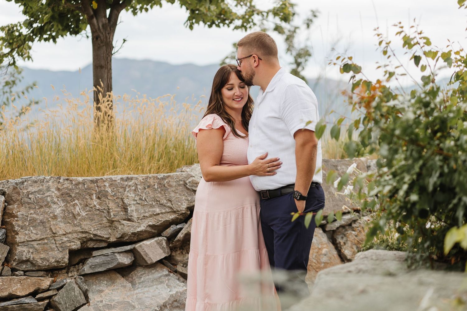 A couple shares a romantic moment during their engagement photoshoot in a scenic mountain landscape at sunset.