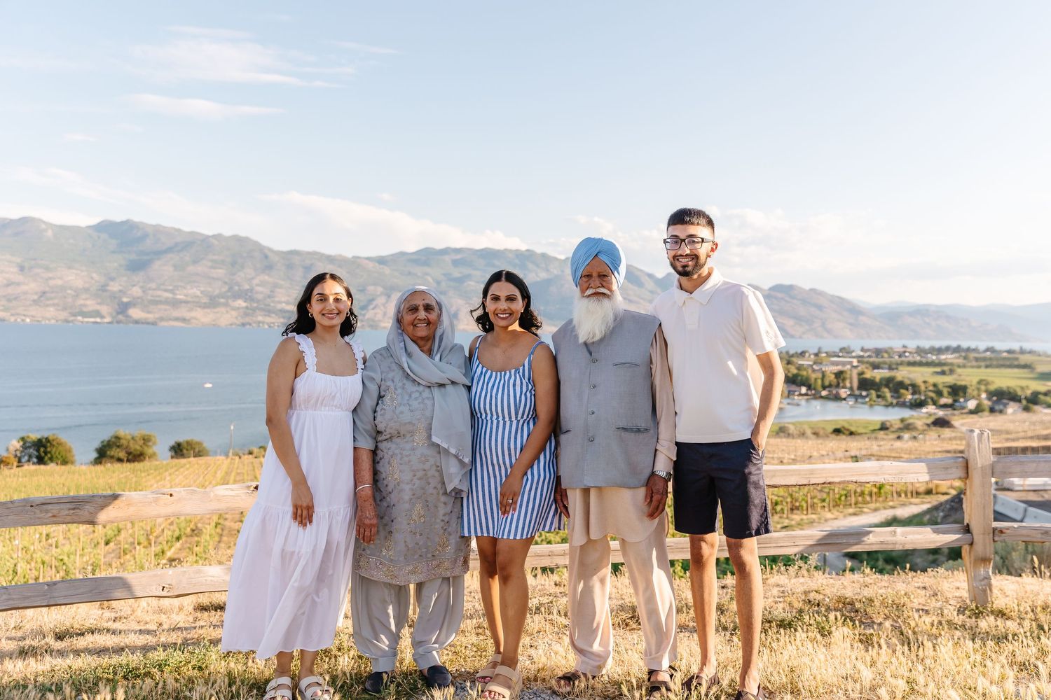 A group of people standing together on a hillside overlooking a scenic lake and mountain landscape on a sunny day.
