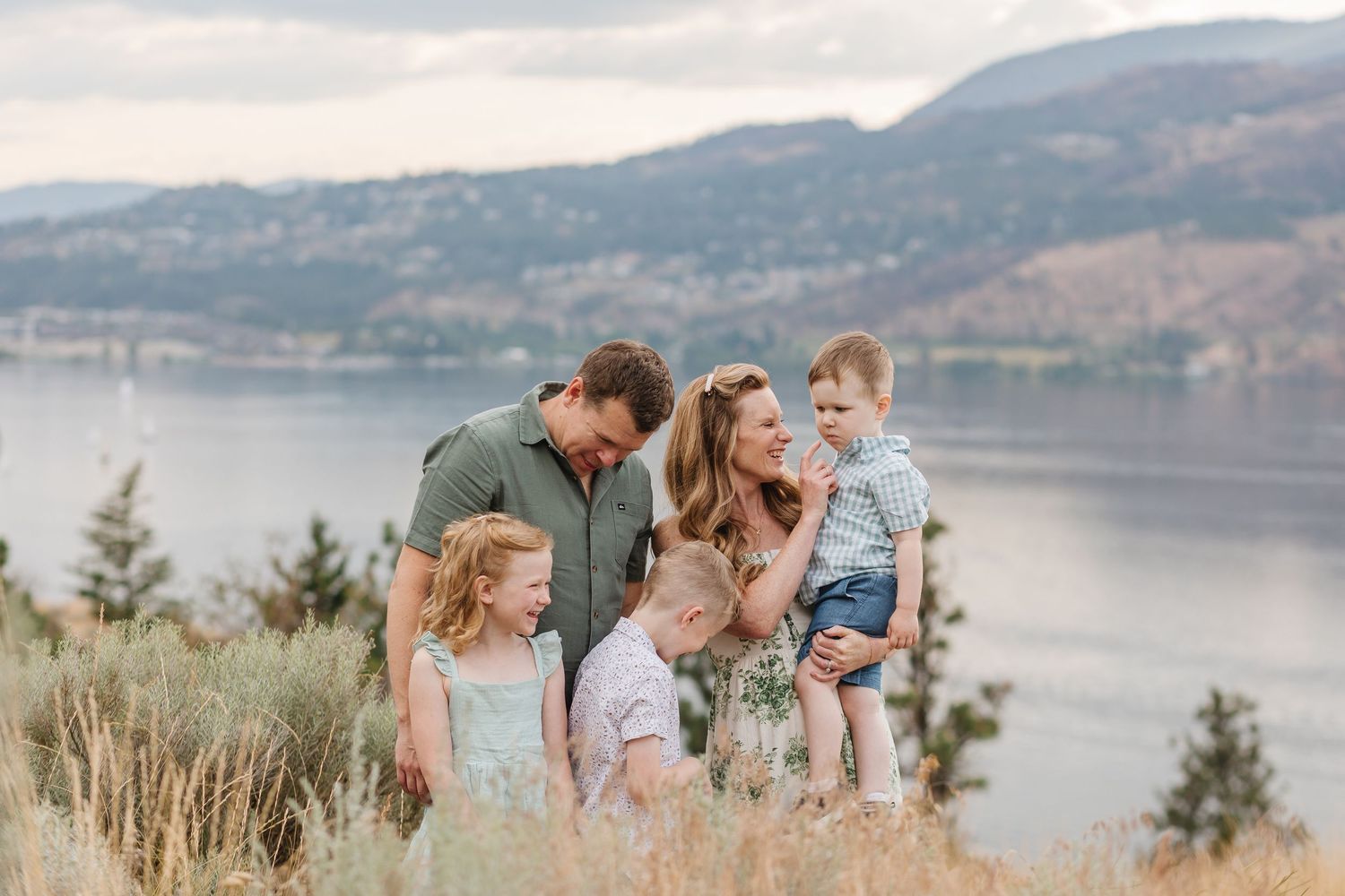 Family enjoying scenic views along a lakeside mountain trail during golden hour with mountains in background.