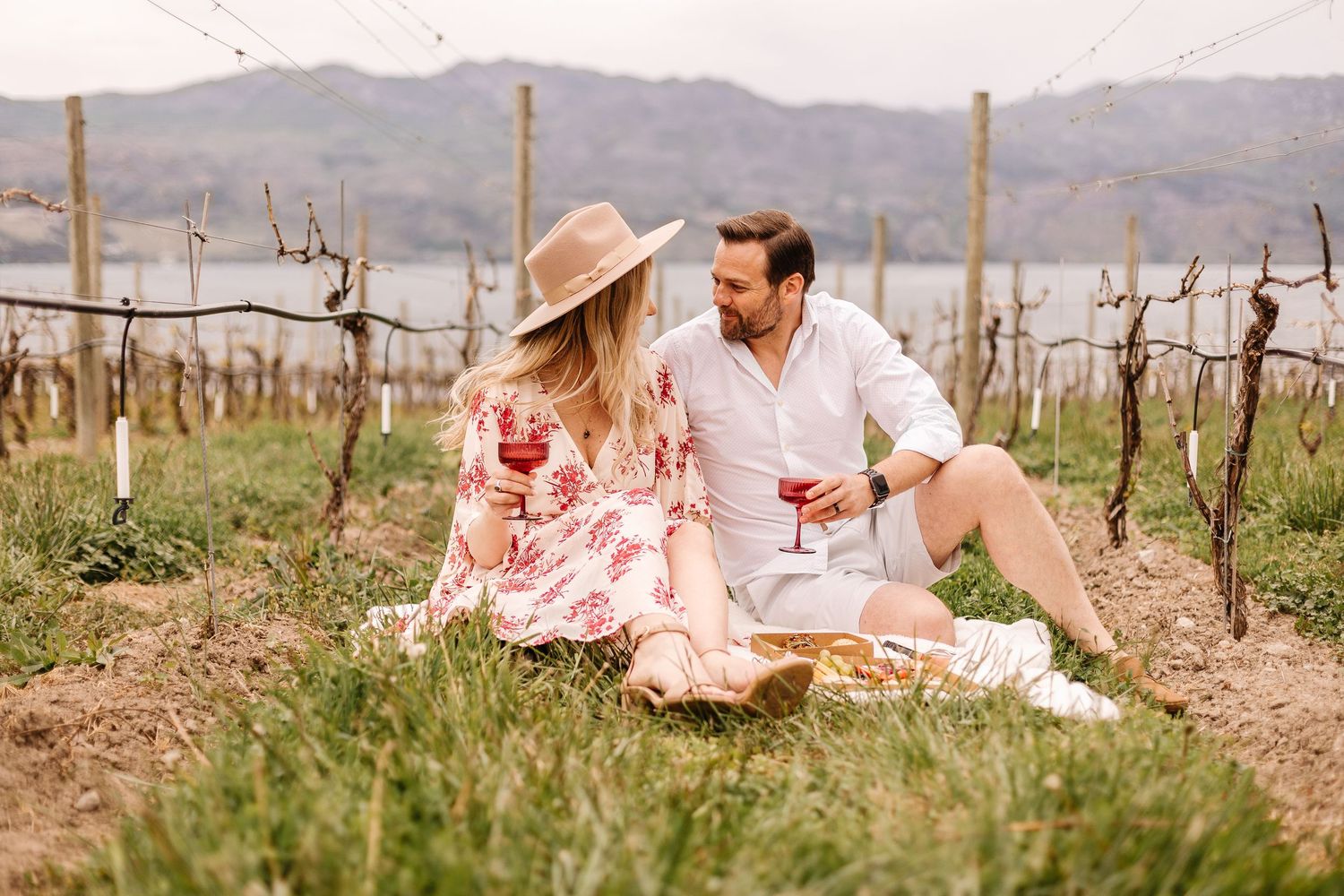 A couple shares a romantic picnic in a vineyard on a sunny afternoon, surrounded by rustic wine country scenery.