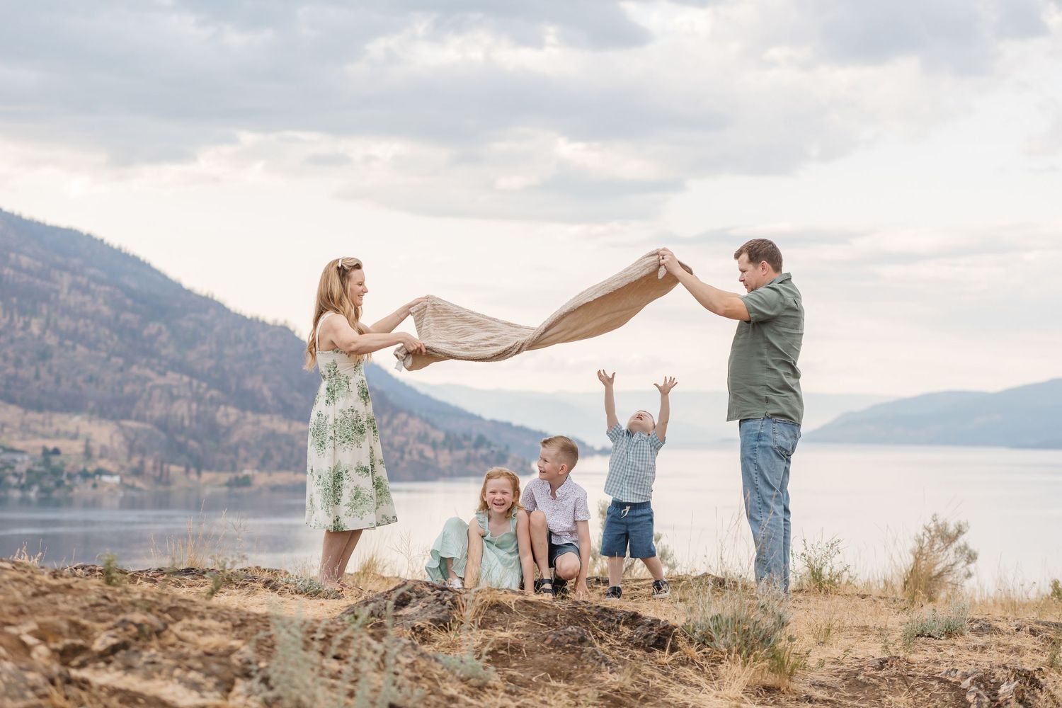 Couple plays with flowing fabric in scenic mountain landscape by lake during golden hour sunset photoshoot.