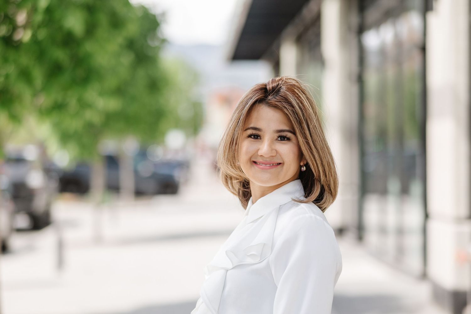 Professional headshot portraits of someone in a white blazer against an outdoor background with blurred greenery.