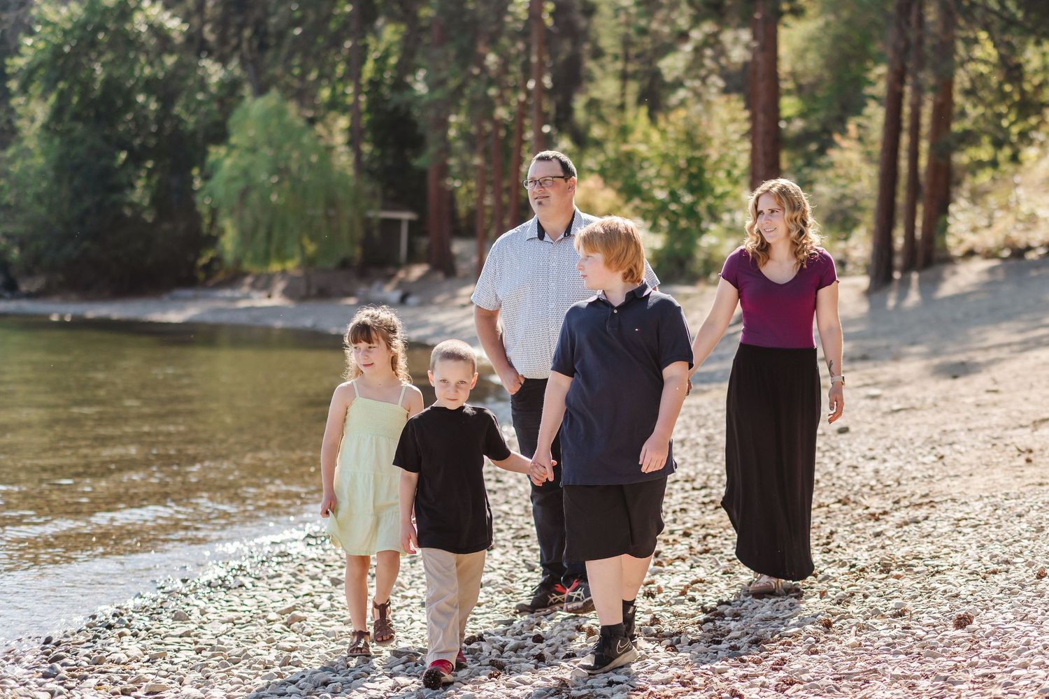Family walking together on a rocky riverbank trail during a sunny summer afternoon.