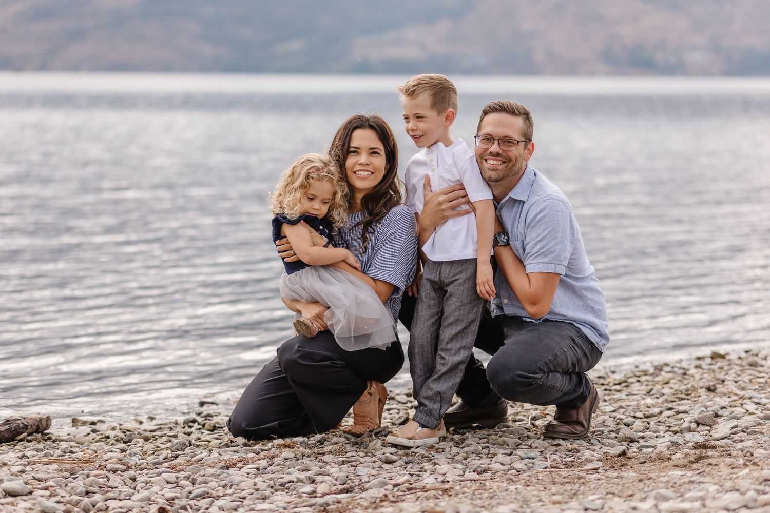 Family in casual attire lying together on a rocky beach at sunset near the water.